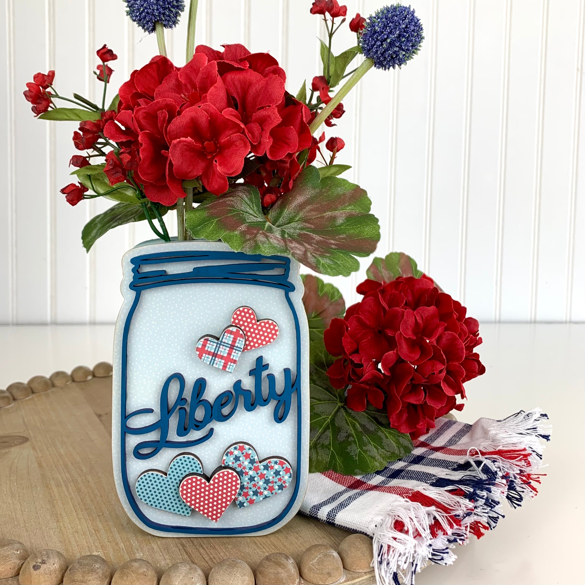 Wood mason jar decoration in red, white, and blue colors with the word liberty on it for 4th of July decorating.  Has a slot in the top to place flowers.