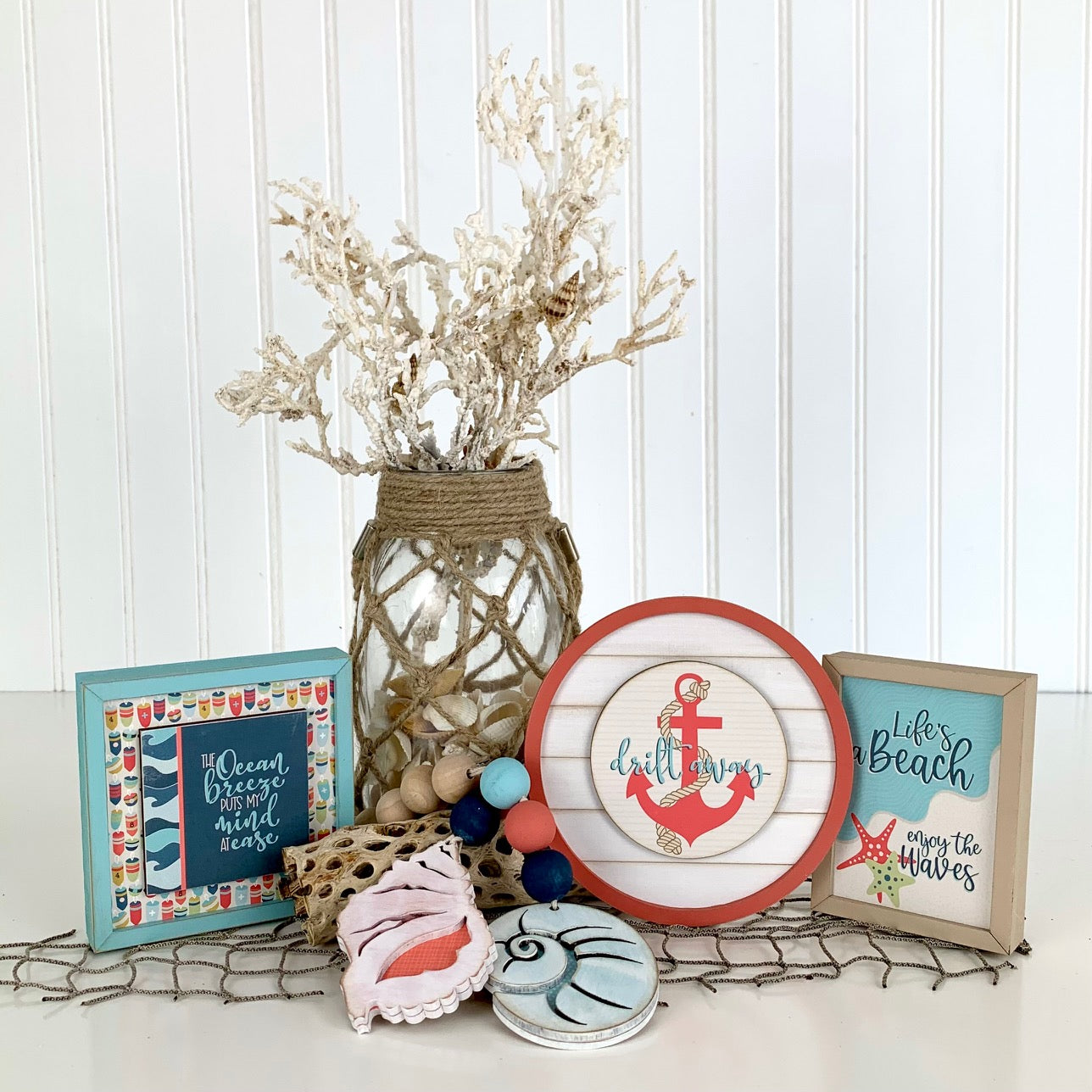 Nautical and beach themed shiplap signs for styling tiered trays, shelves, and mantels. Wood beaded garland with blue and coral seashells. Shiplap sign sign with anchor. Sign life's a beach, enjoy the waves. Drift away sign.