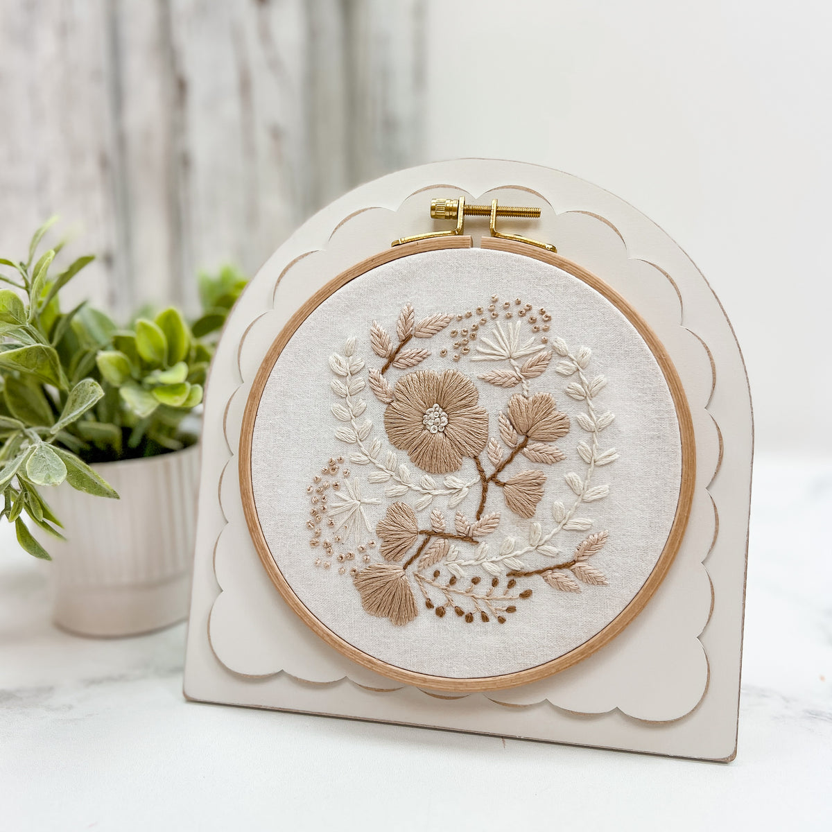 Pre-painted arched scallop embroidery and cross stitch frame with a neutral finish, holding a round floral embroidery hoop and displayed with an easel stand.