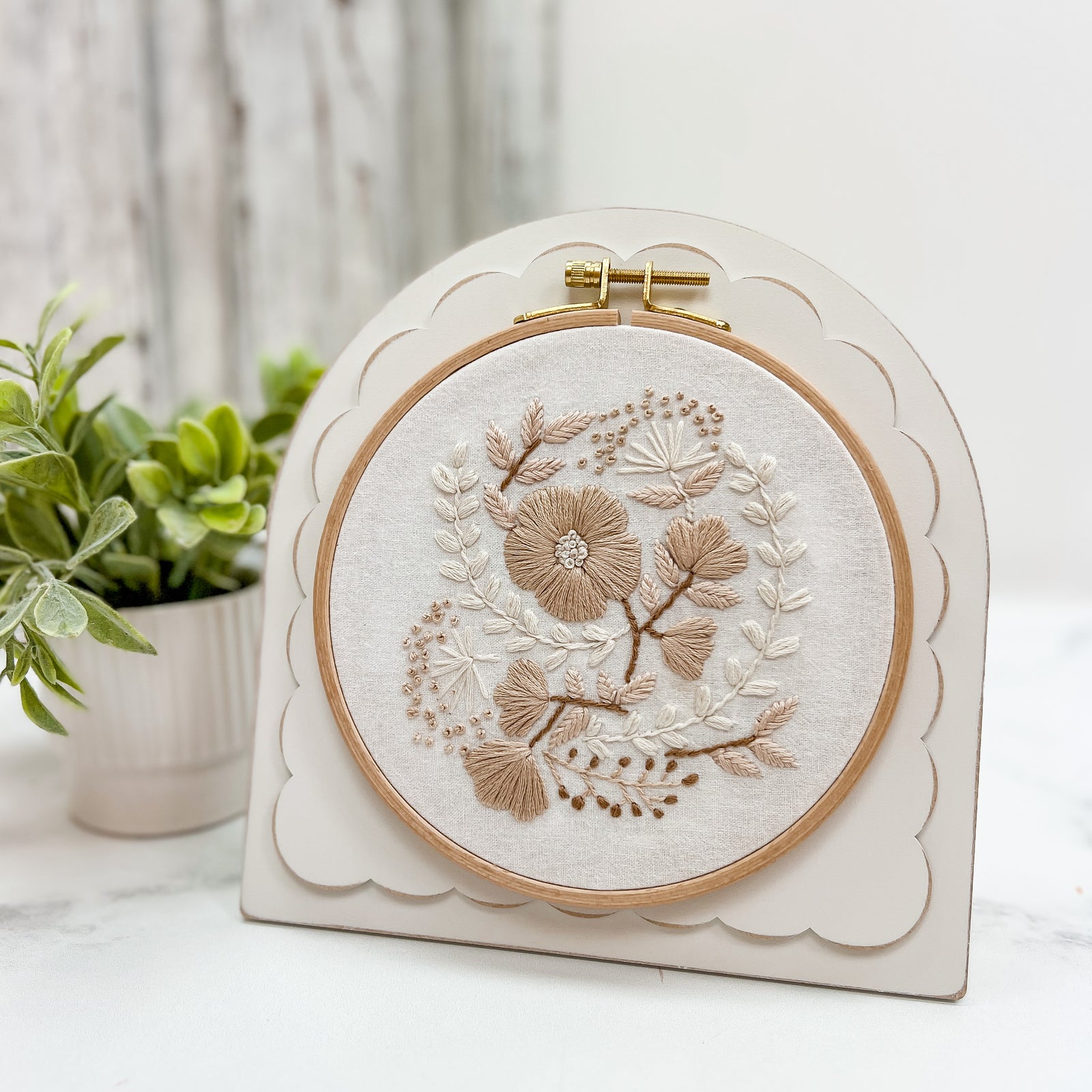 Pre-painted arched scallop embroidery and cross stitch frame with a neutral finish, holding a round floral embroidery hoop and displayed with an easel stand.