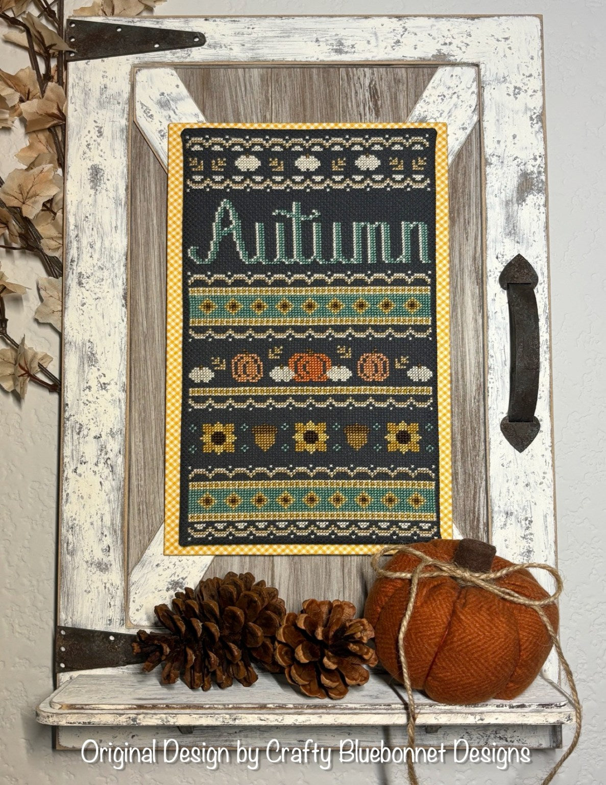 Decorative sign with 'Autumn' text and fall sampler pumpkins, sunflowers, acorns and leaves cross-stitch pattern on a prairie porch shelf wooden frame
