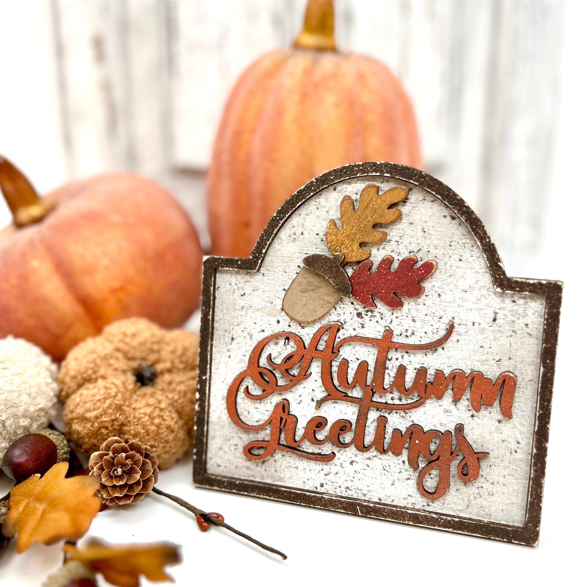 Decorative sign with 'Autumn Greetings' text surrounded by pumpkins and leaves on a white background