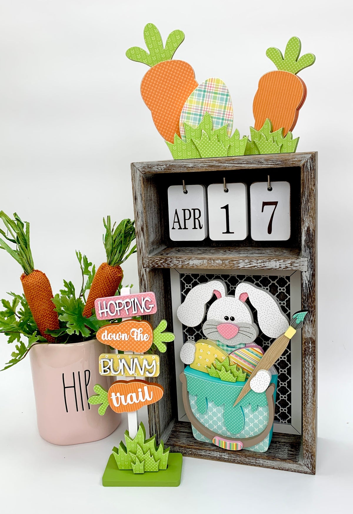 Easter wood sign that says hopping down the bunny trail and an Easter bunny painting eggs.