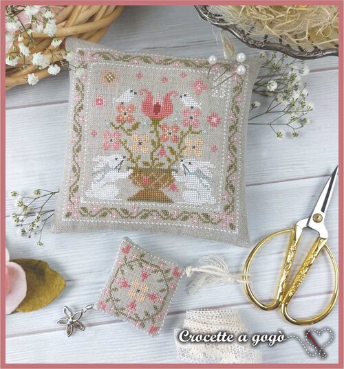 Cross-stitched pillow with white bunnies and floral design with a separate scissor fob floral chart.