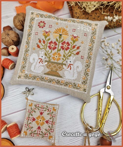 Cross-stitched pillow with floral design framed by two squirrels along with a scissor fob featuring an autumnal floral quilt design