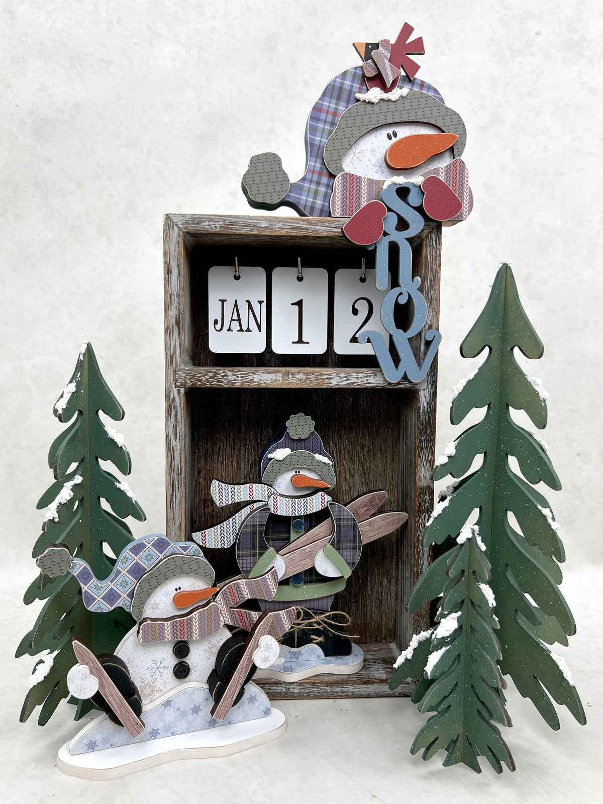 calendar box decorated with a winter theme. Snowman holding skiis, sitting snowman with skiis, and snowman head holding the word snow.