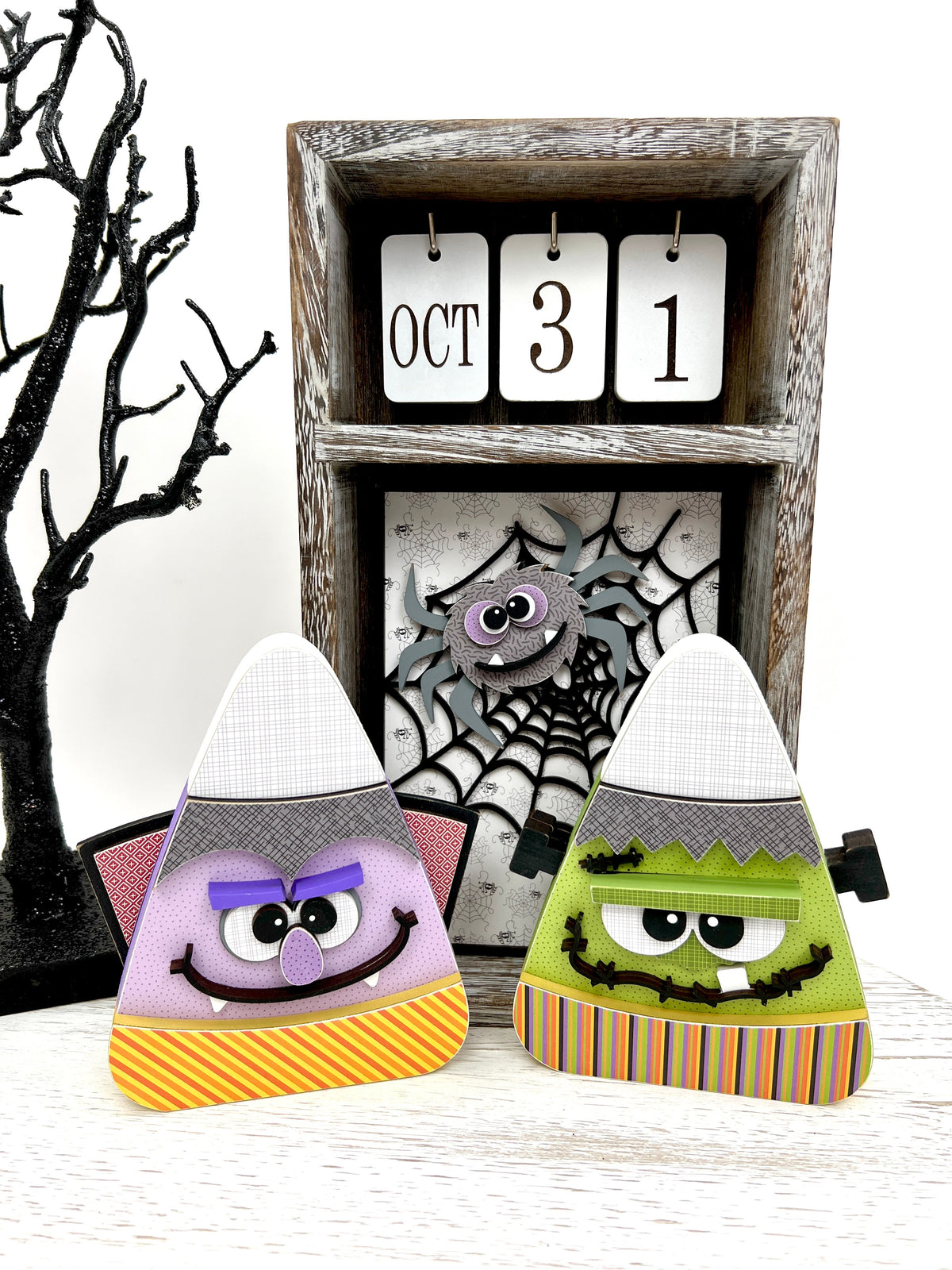 Candy corn shaped wood decorations that look like frankenstein and dracula with a calendar box with a spider web and spider/.