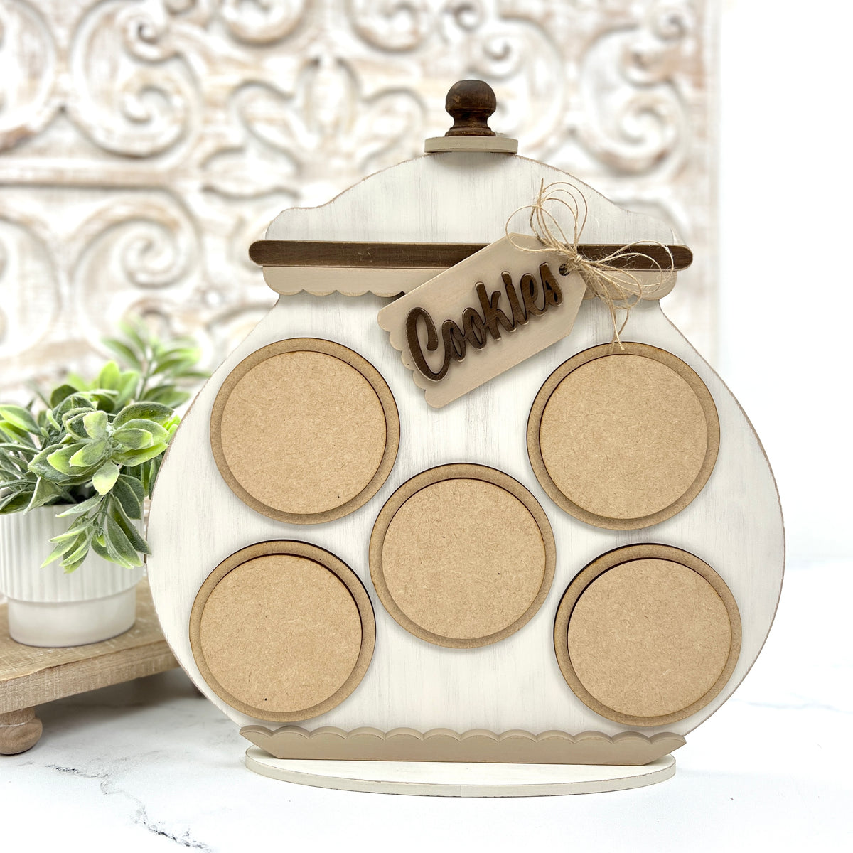 Whimsical unfinished wood cookie jar shaped cross stitch display with round inset openings for interchangeable stitched designs and decorative tag.