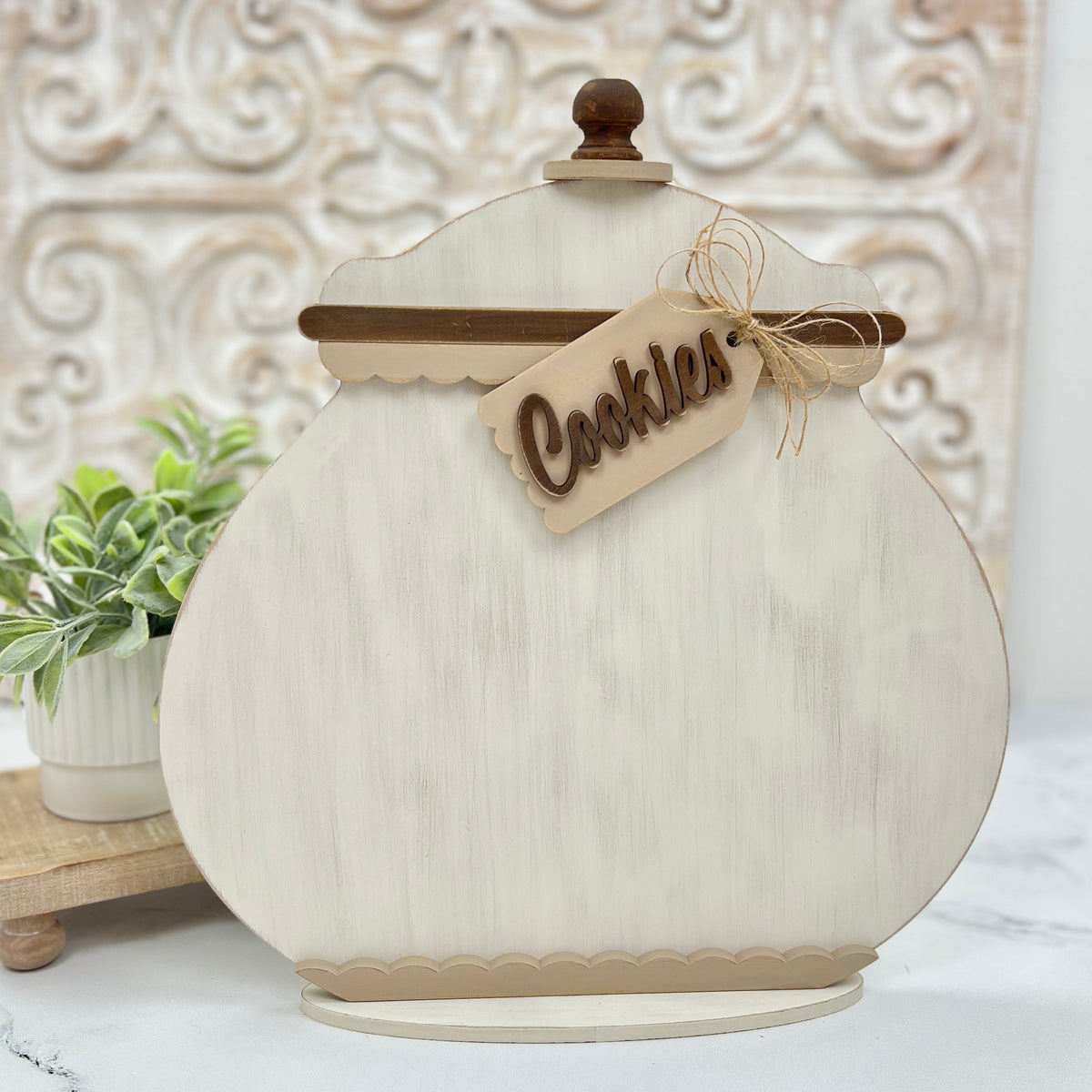 Decorative cookie jar with a 'Cookies' tag on a white surface with a decorative wall in the background.