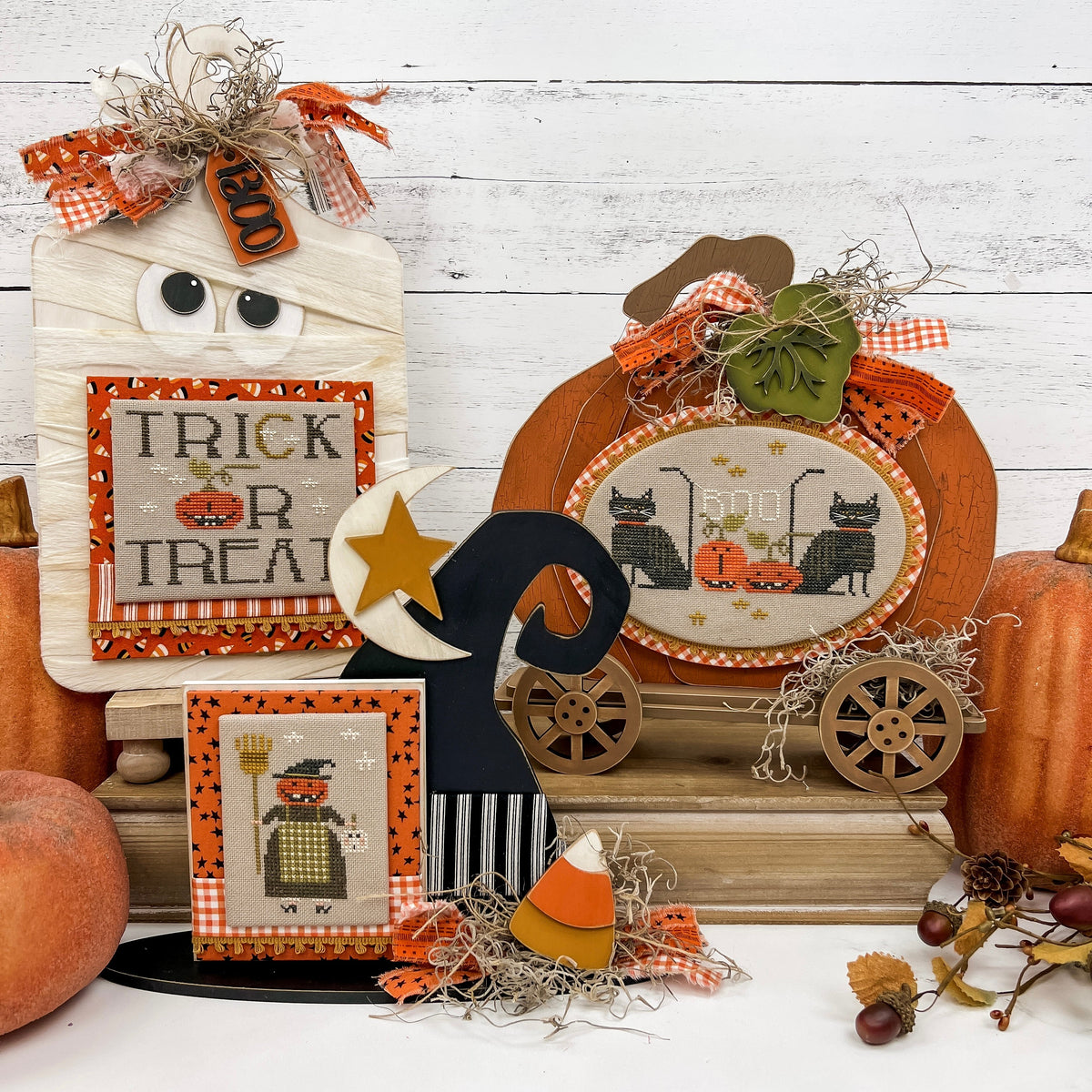 Halloween themed cross stitch display boards; mummy, witch hat, and primitive pumpkin with wheels. Finished halloween cross stitch designs by Brenda Gervais.