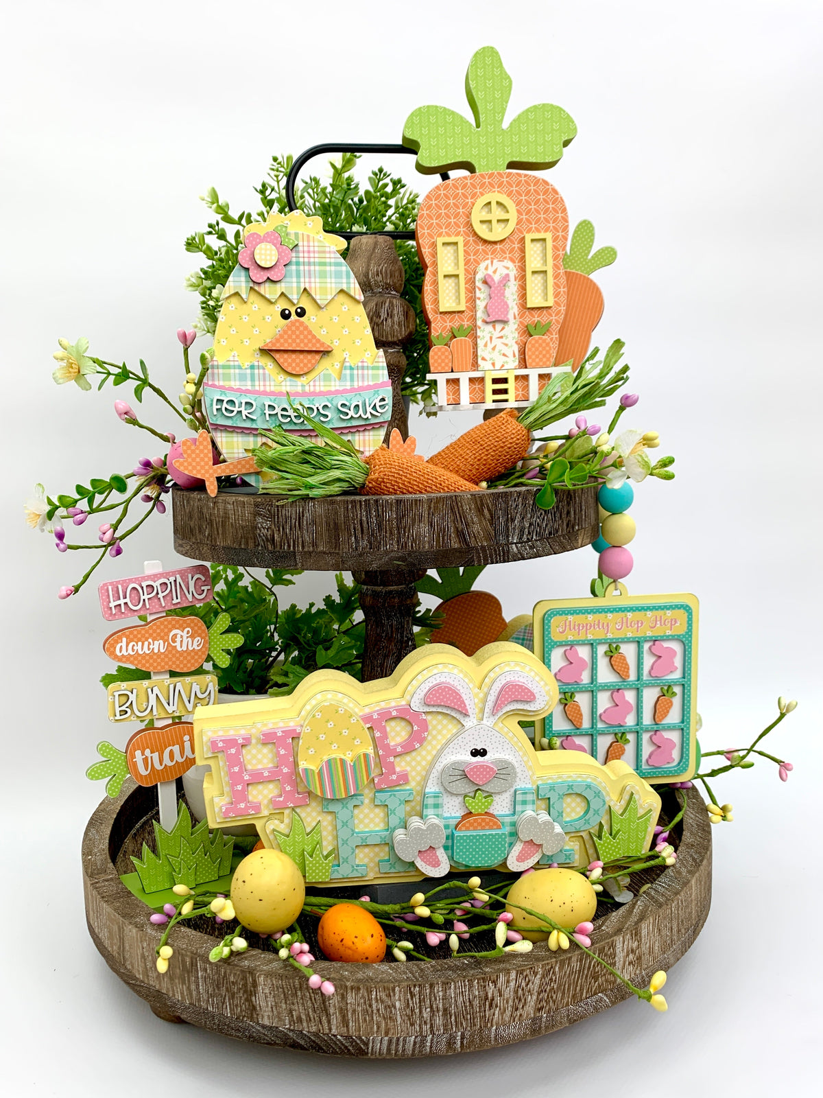 Easter tiered tray decorations.  Easter chick inside a cracked egg, hop easter bunny, carrot house, and wood beaded carrot garland.