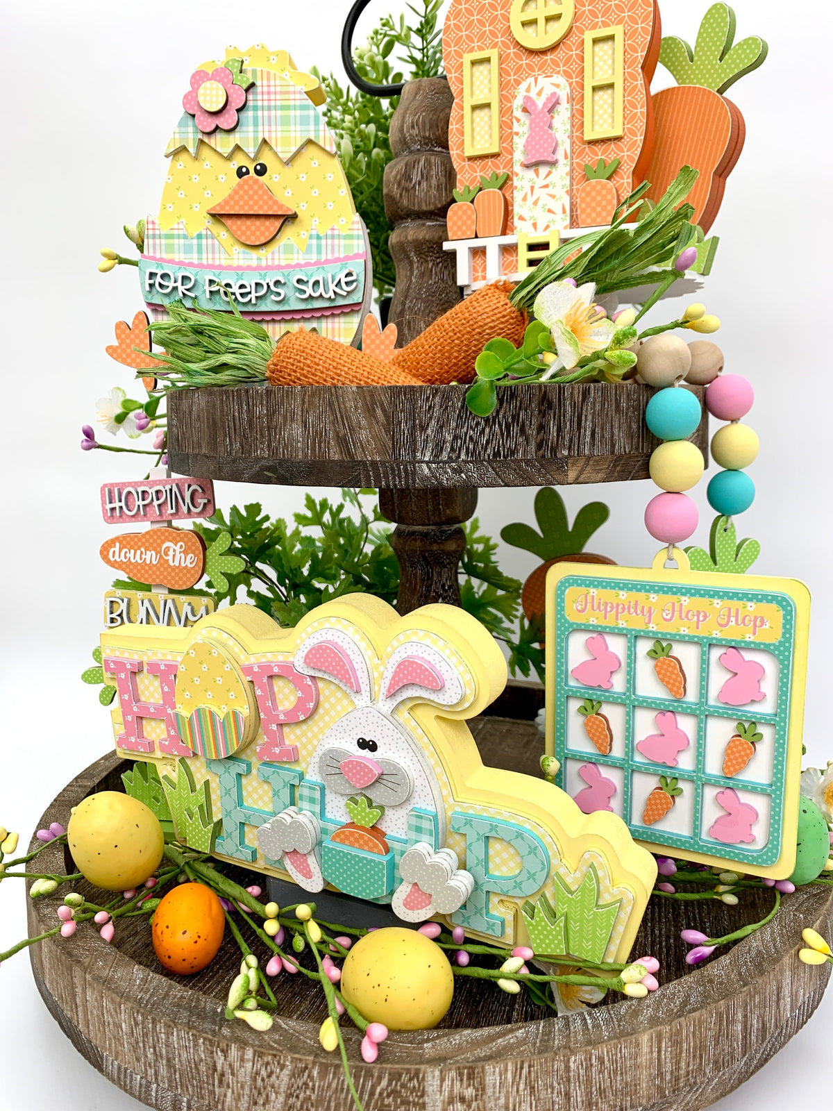 Easter tiered tray decorations.  Easter chick inside a cracked egg, hop easter bunny, carrot house, and wood beaded carrot garland.