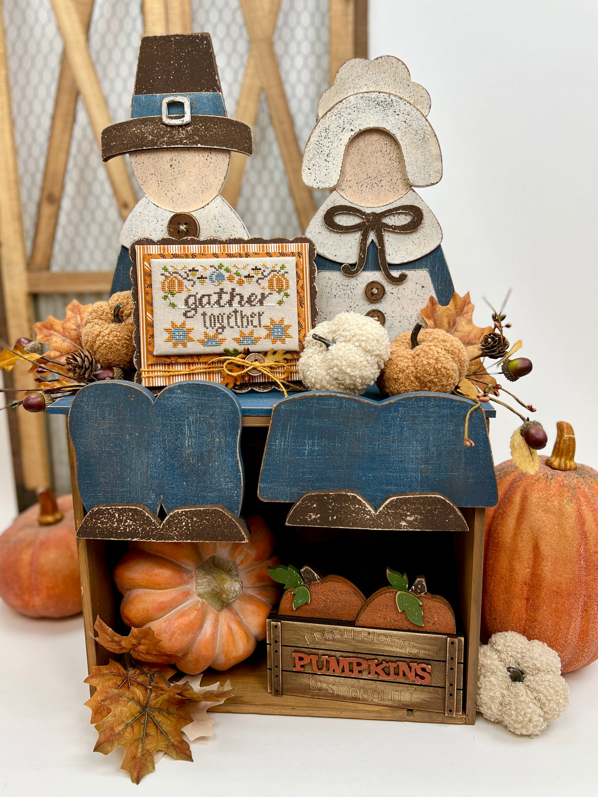Decorative display with pilgrim figures, pumpkins, and a sign that says &#39;gather together&#39; on a white background.