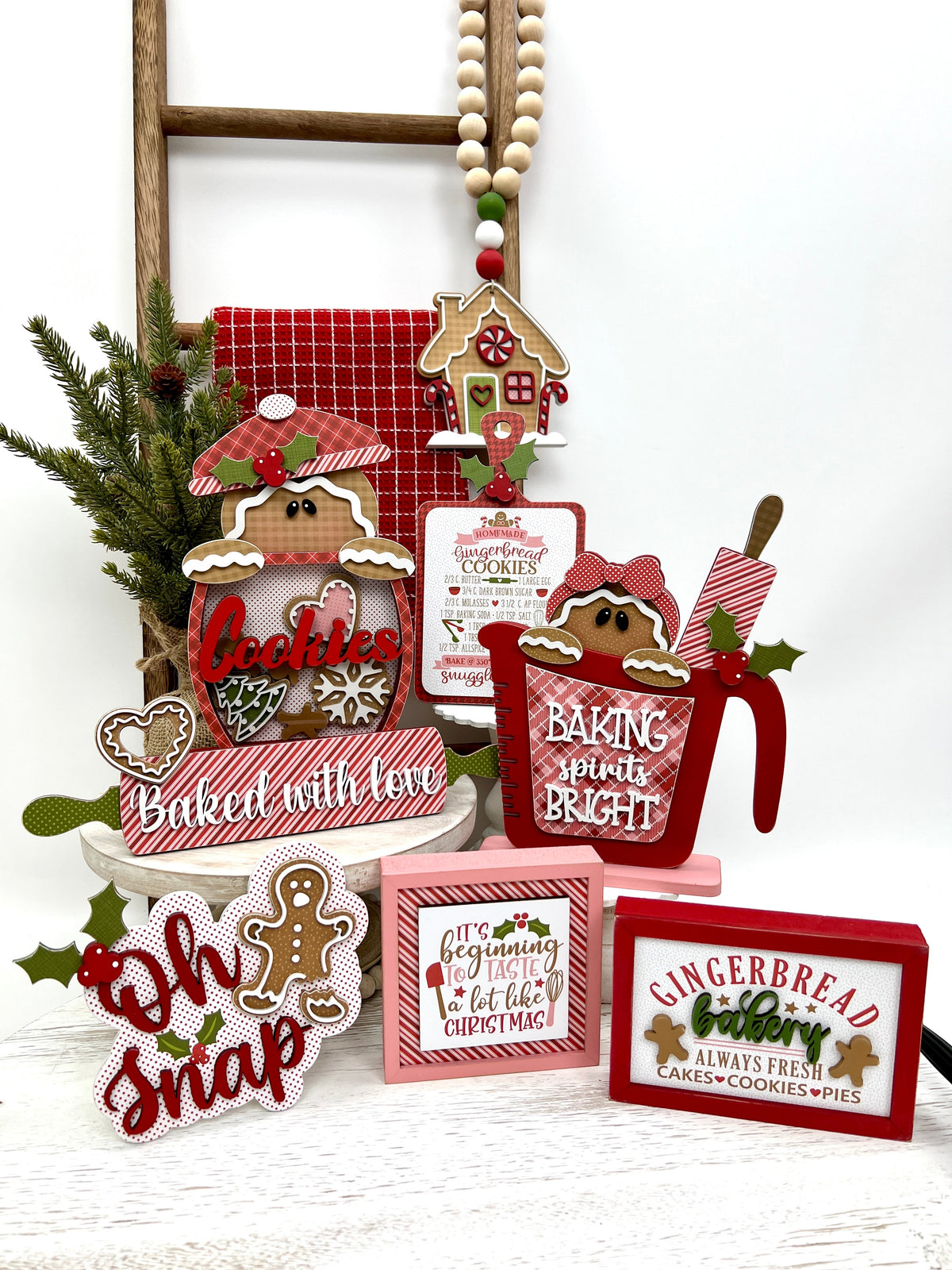 Christmas gingerbread wood decorations with cookie jar, gingerbread girl in measuring cup, recipe board, baked with love rolling pin, and wood beaded gingerbread house garland.