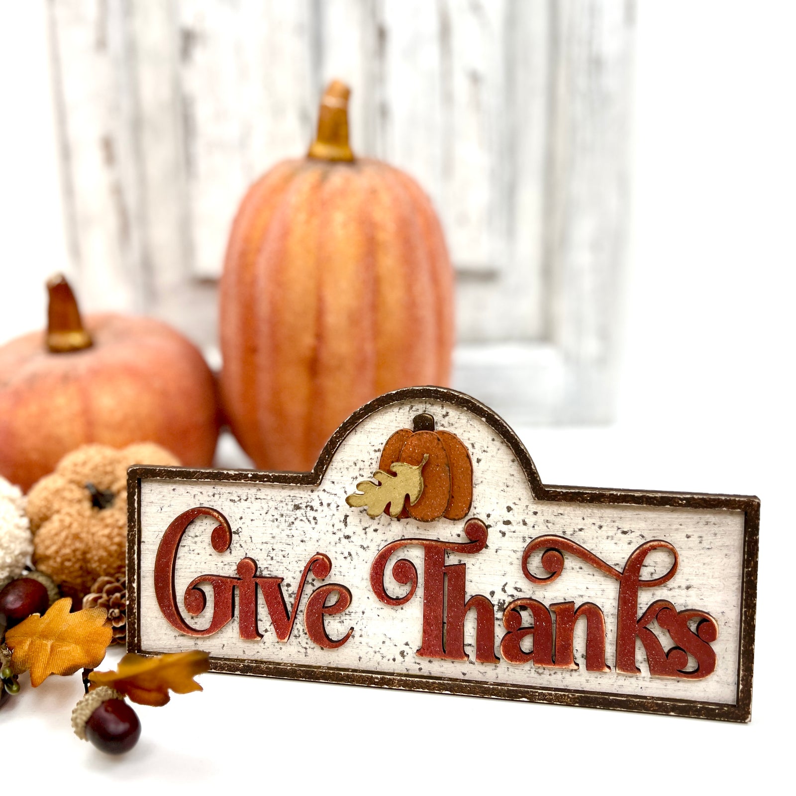 Decorative sign with 'Give Thanks' text and pumpkins in the background