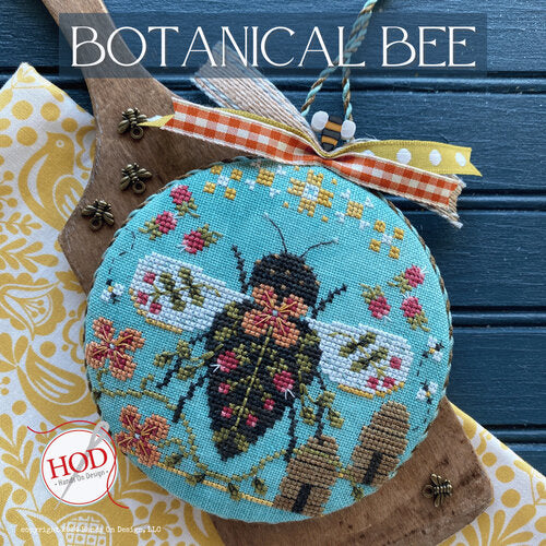 Cross Stitch round with bee design on a blue background with bee hives and flowers