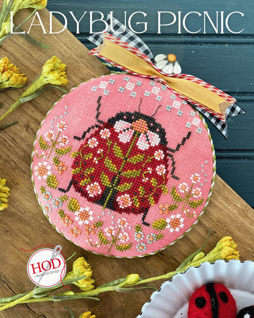 Cross-stitched ladybug design on a pink fabric with daisy flowers