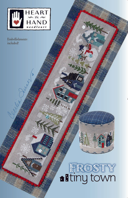 Cross-stitched design of a snowy village with trees and houses and a jolly snowman.