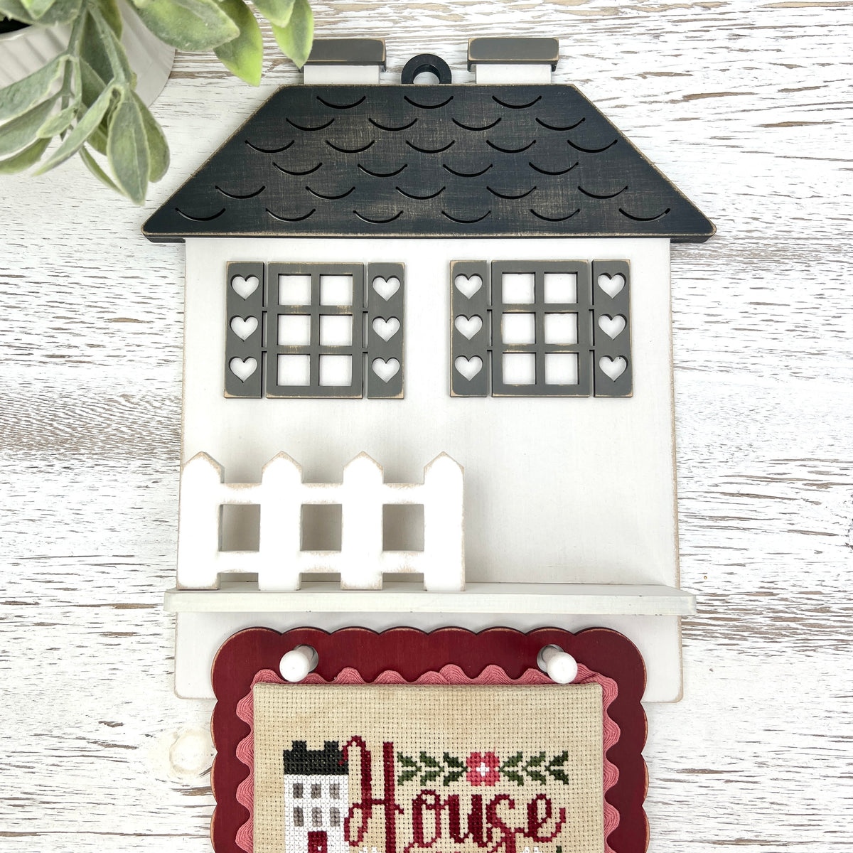 House Rules cottage DIY cross stitch display with heart shutters, picket fence shelf, and hanging pegs