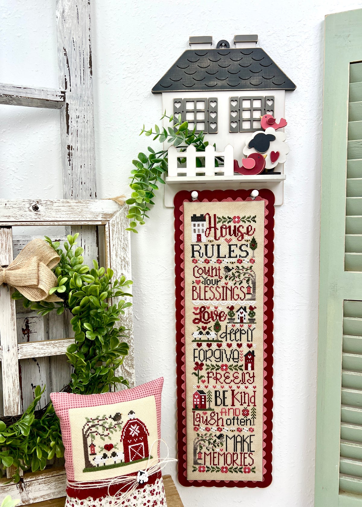 House Rules cottage DIY cross stitch display with heart shutters, picket fence shelf,  hanging pegs, and House Rules cross stitch by Primrose Cottage.