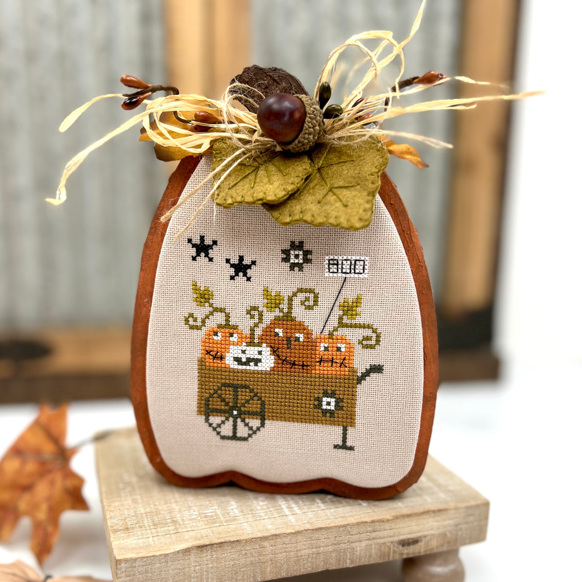 Decorative pumpkin with cross-stitched design on a wooden pumpkin stand