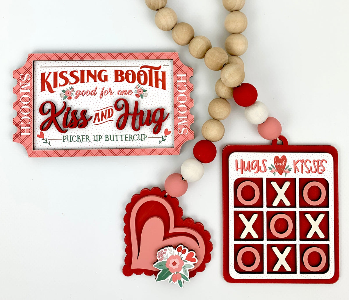 Valentine wood decor craft kit with a kssing booth ticket and a beaded garland with a pink and red heart and a hugs and kisses tic tac toe.