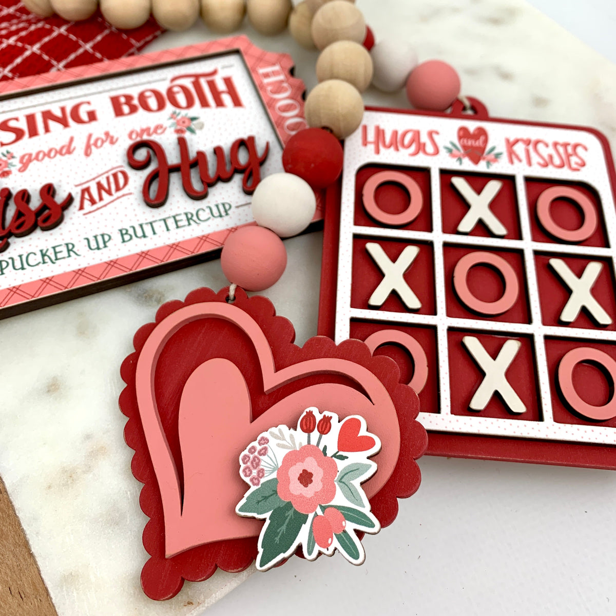 Valetine wood decorations for tiered tray styling in pink and red with a heart, kissing booth ticket and a hugs and kisses tic tac toe