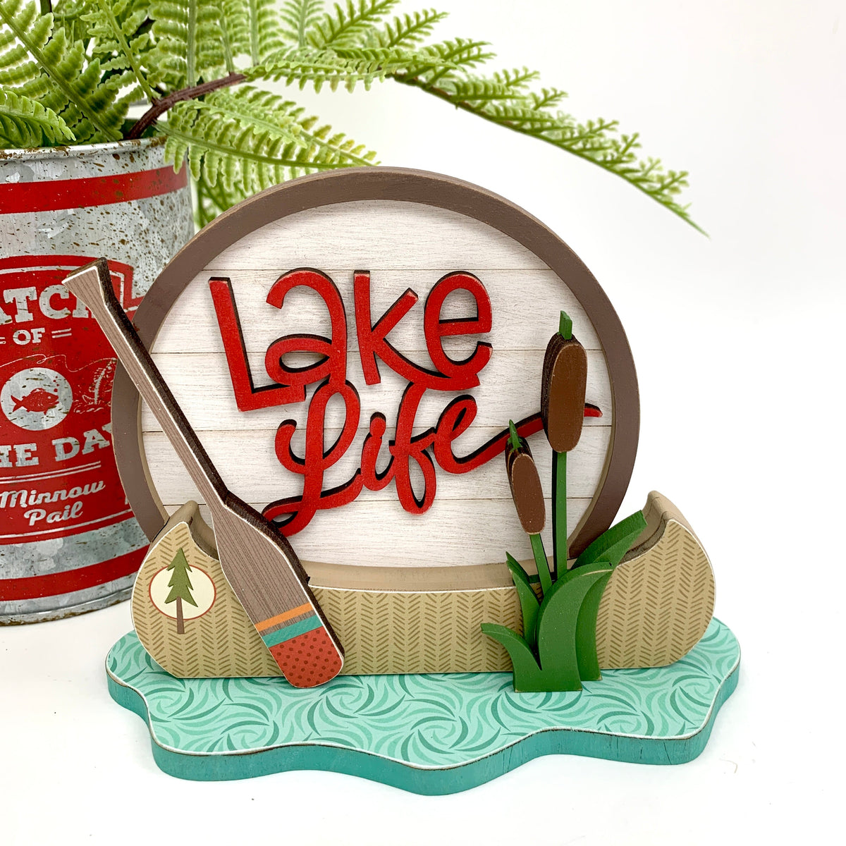 Small wood decor sign that says lake life with a wood canoe, oar, water, and cattails