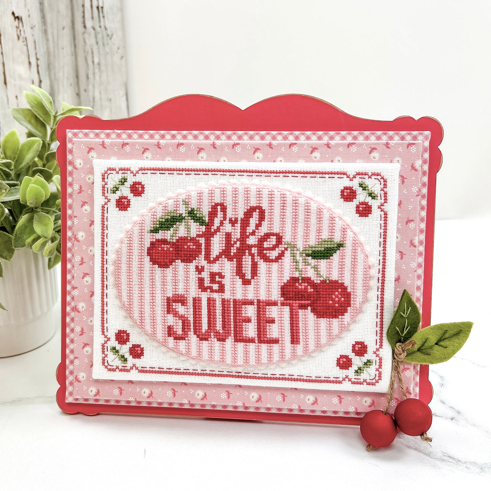 Fully painted Life is Sweet cherry cross stitch display kit with red lettering, stitched cherries, dimensional cherry embellishment, and included pattern.