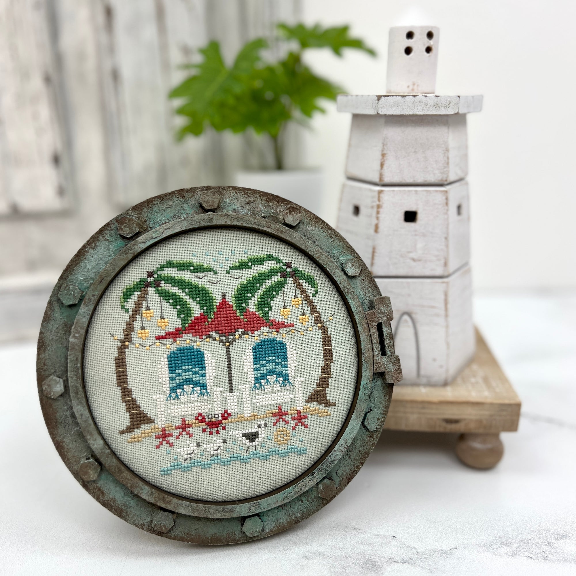 DIY round nautical porthole wood frame with patina finish, displaying a tropical cross stitch design, styled with coastal décor accents.
