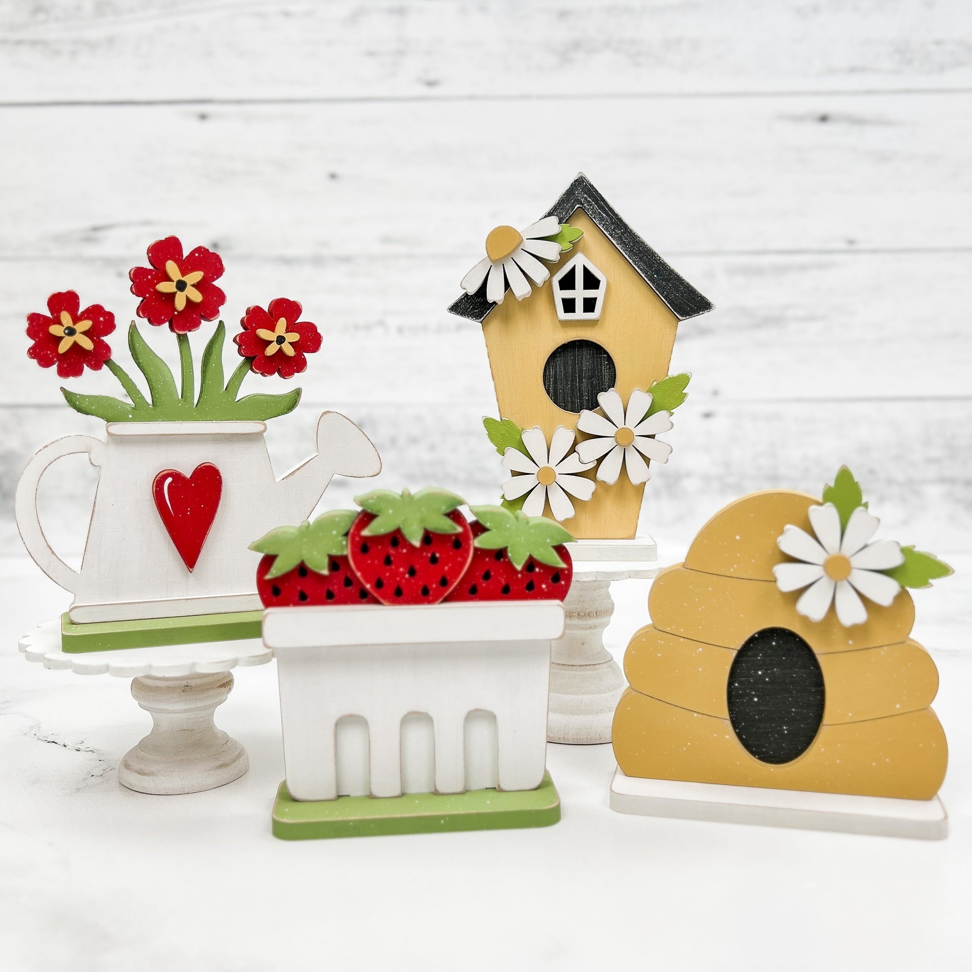 spring and summer wood craft shapes; water can with red flowers, yellow birdhouse with daiseys, strawberry basket, and bee hive. 