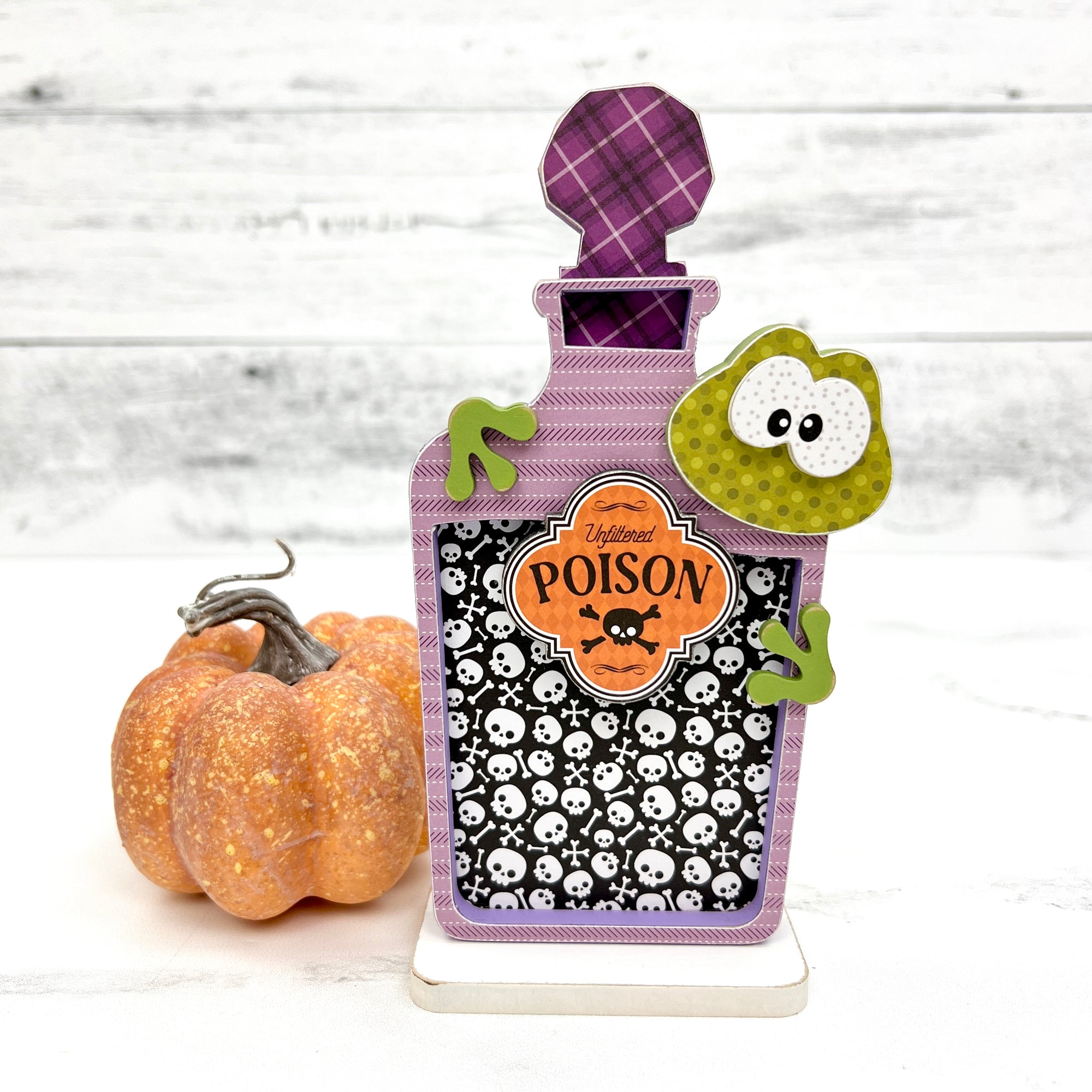 Green toad peeking over the side of an apothecary bottle. DIY Halloween wood craft kit.