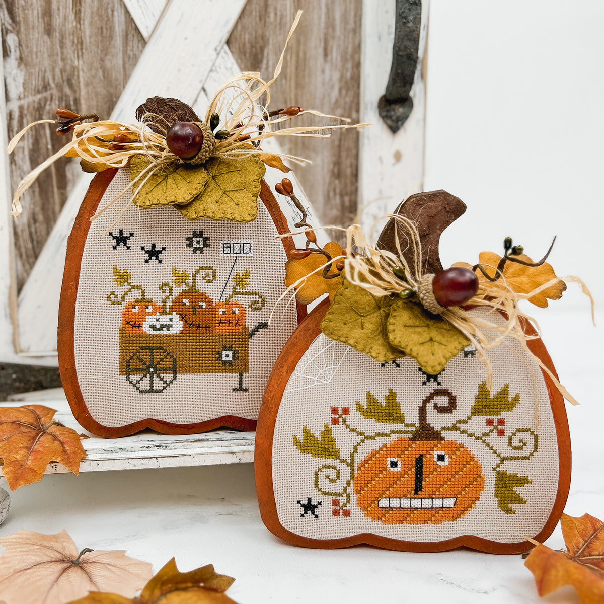 Decorative pumpkins with cross-stitch designs on a wooden pumpkin background. Cross stitch pattern Happy Halloween by Crocette a gogo.