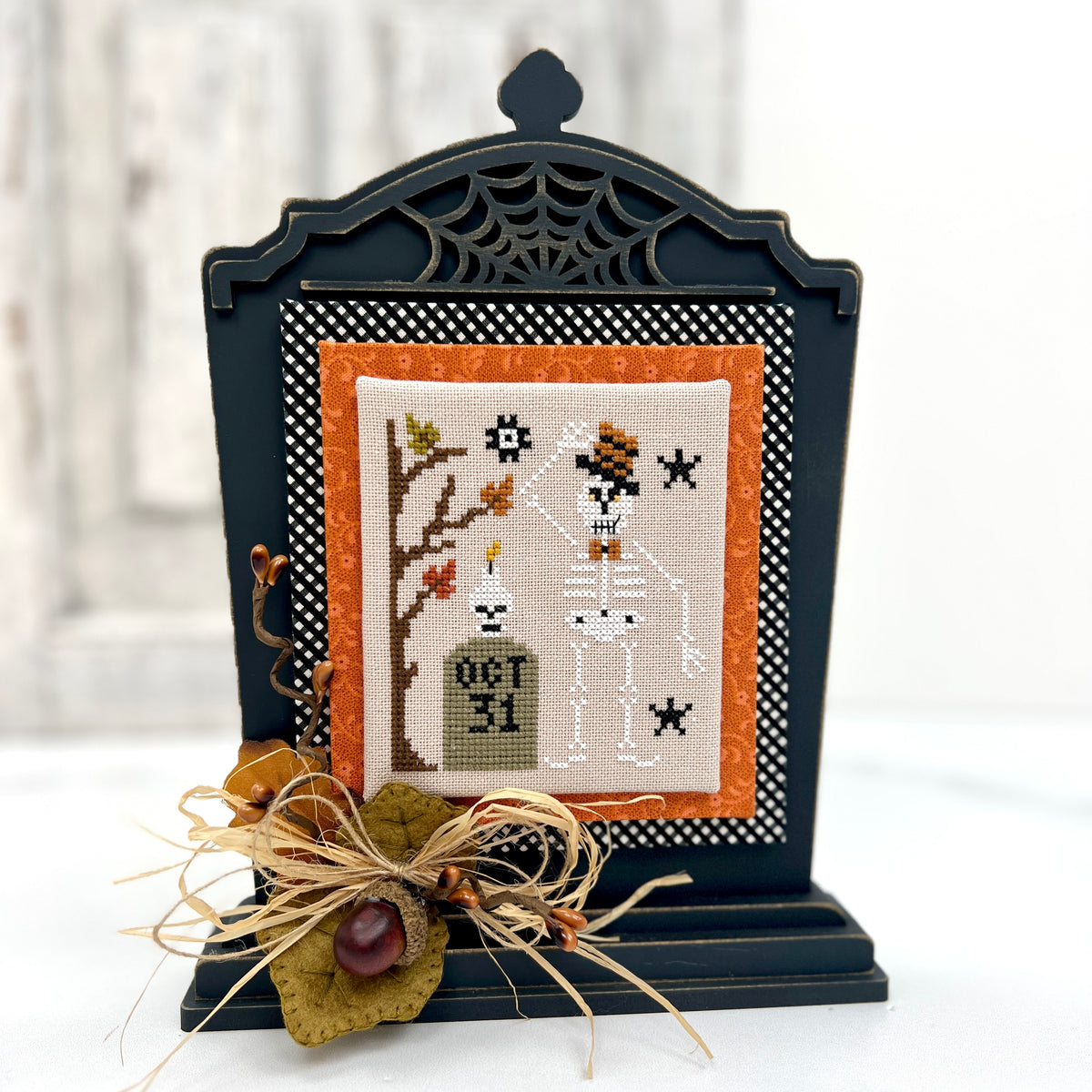 Decorative Halloween cross-stitch piece in a black frame with spiderweb design.