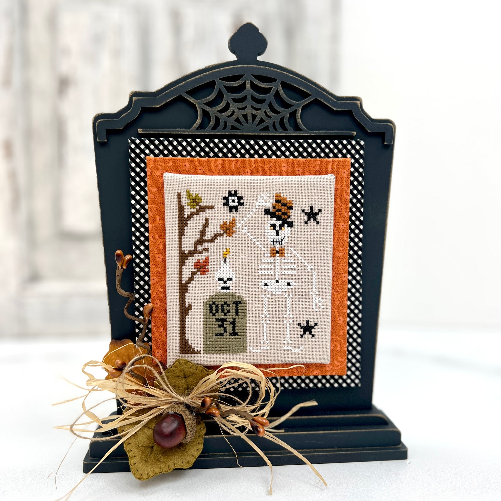 Decorative Halloween cross-stitch piece in a black frame with spiderweb design.