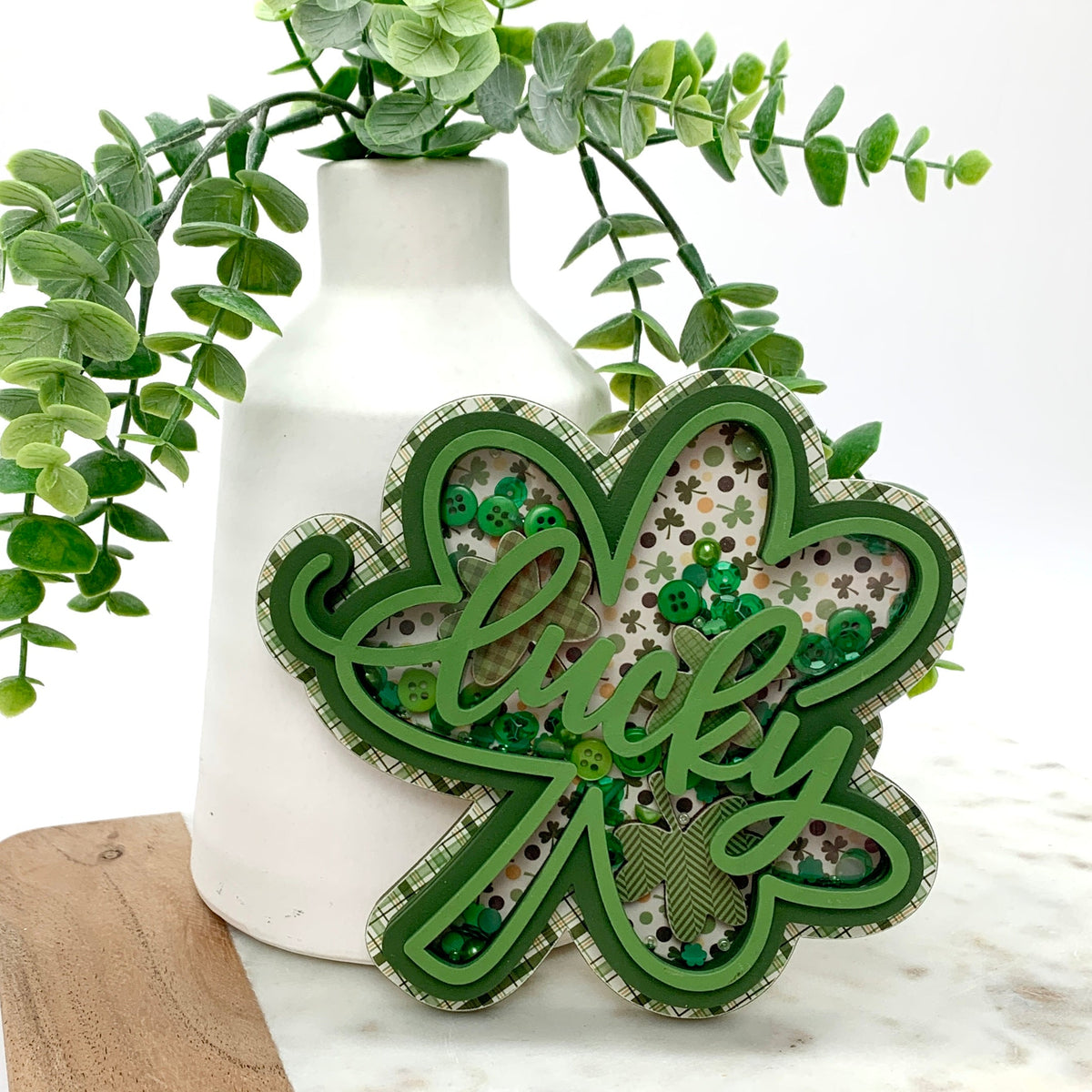 Green wood shamrock with the word lucky filled with confetti and sequins.
