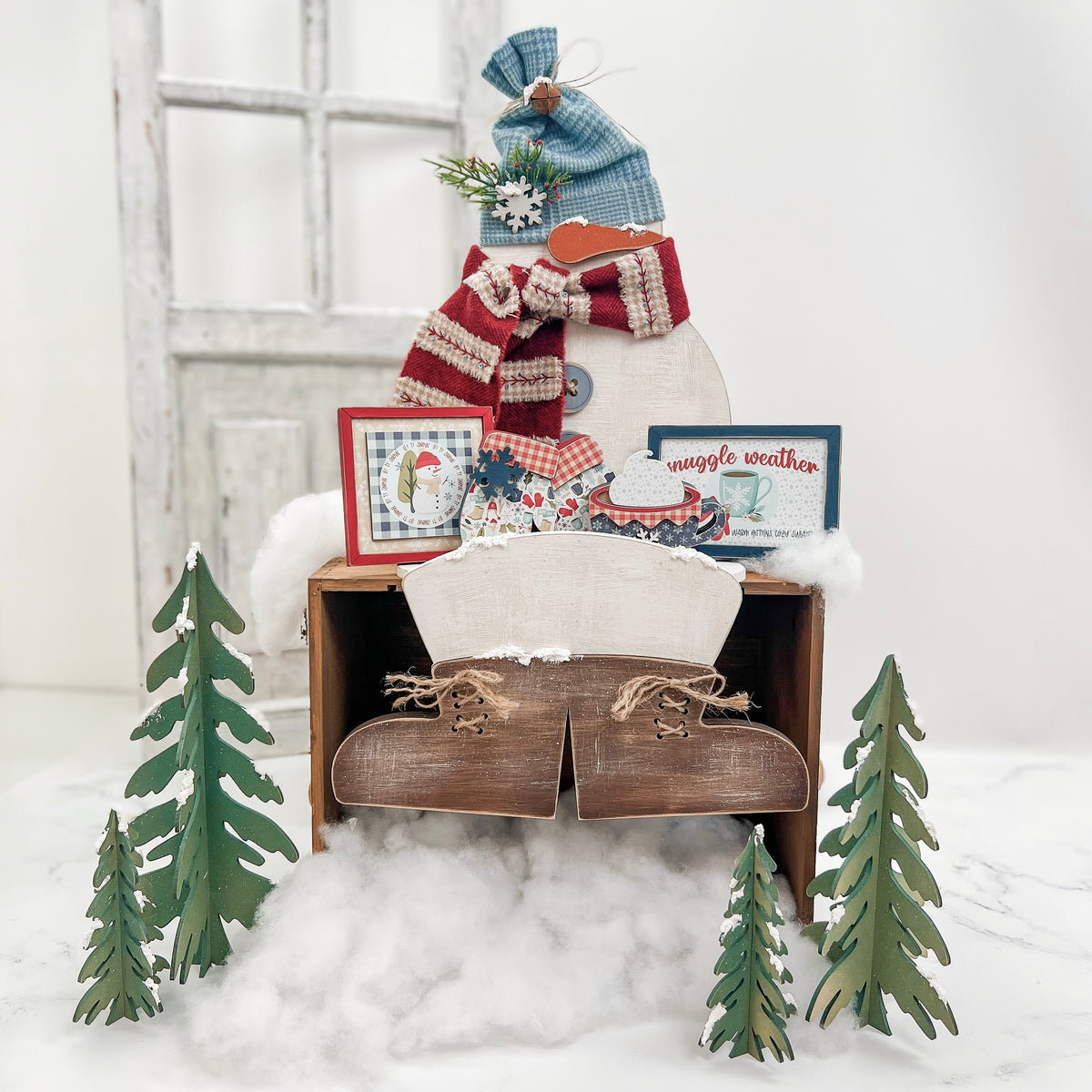 Snowman shelf made of unfinished wood, styled with winter chunky shapes, framed signs, faux snow, and seasonal décor, designed to display finished cross stitch pieces and small wood accents.