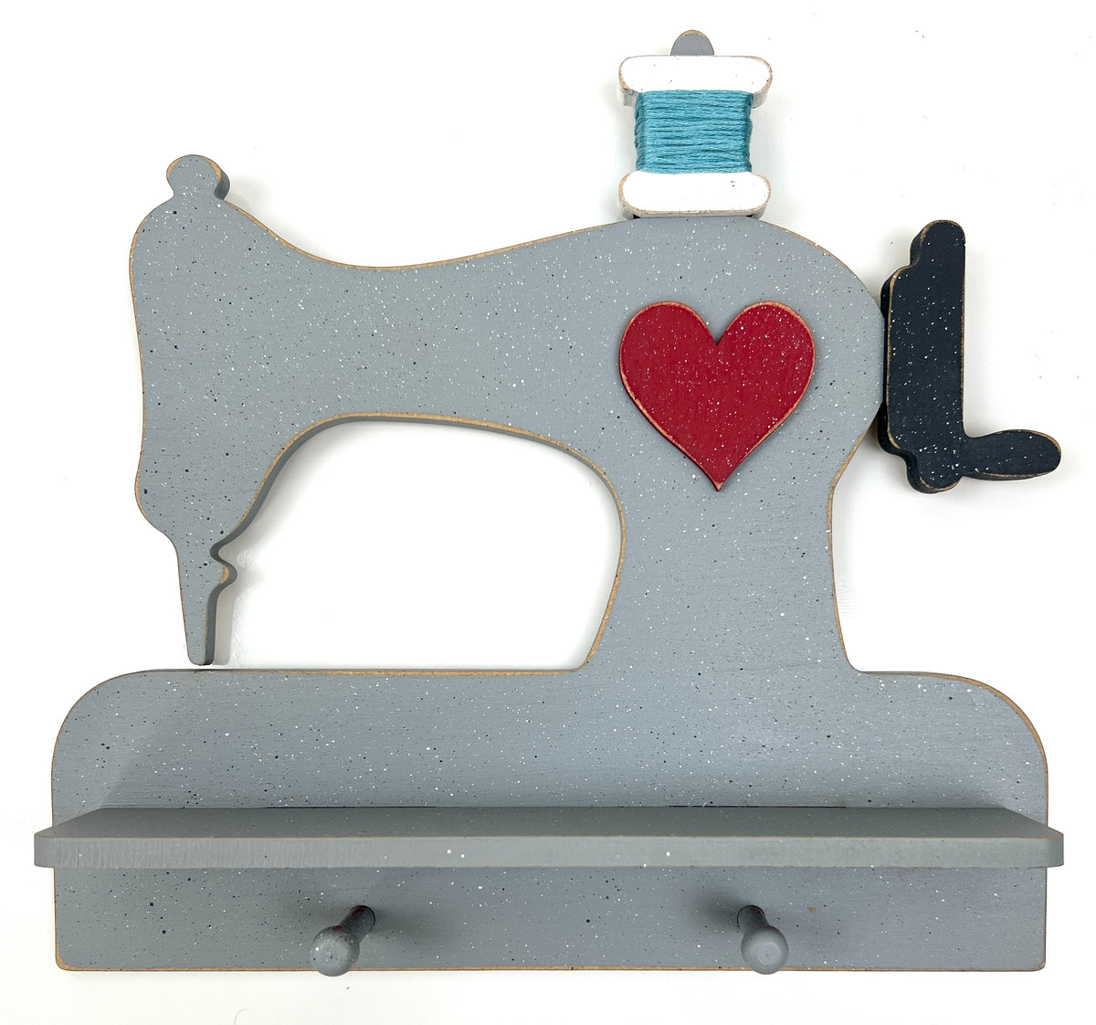 A decorative gray wooden sewing machine wall sign with a red heart and a blue spool of thread detail, shown against a plain white background.