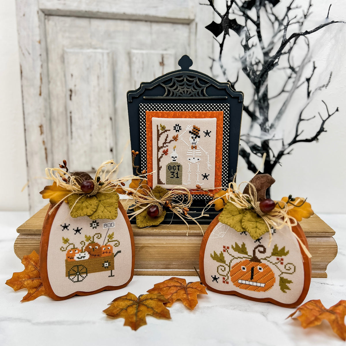 Decorative Halloween pumpkins with cross-stitch designs and a black tombstone in the background.