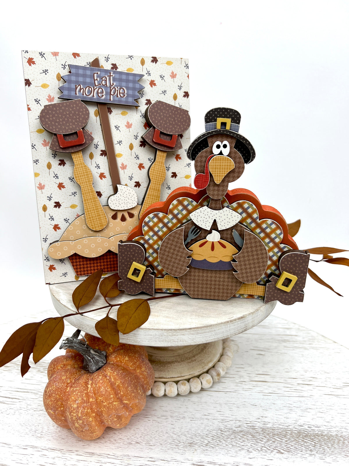 Sitting turkey eating pie and a turkey with legs coming out of a pie decoration on a white pedestal stand