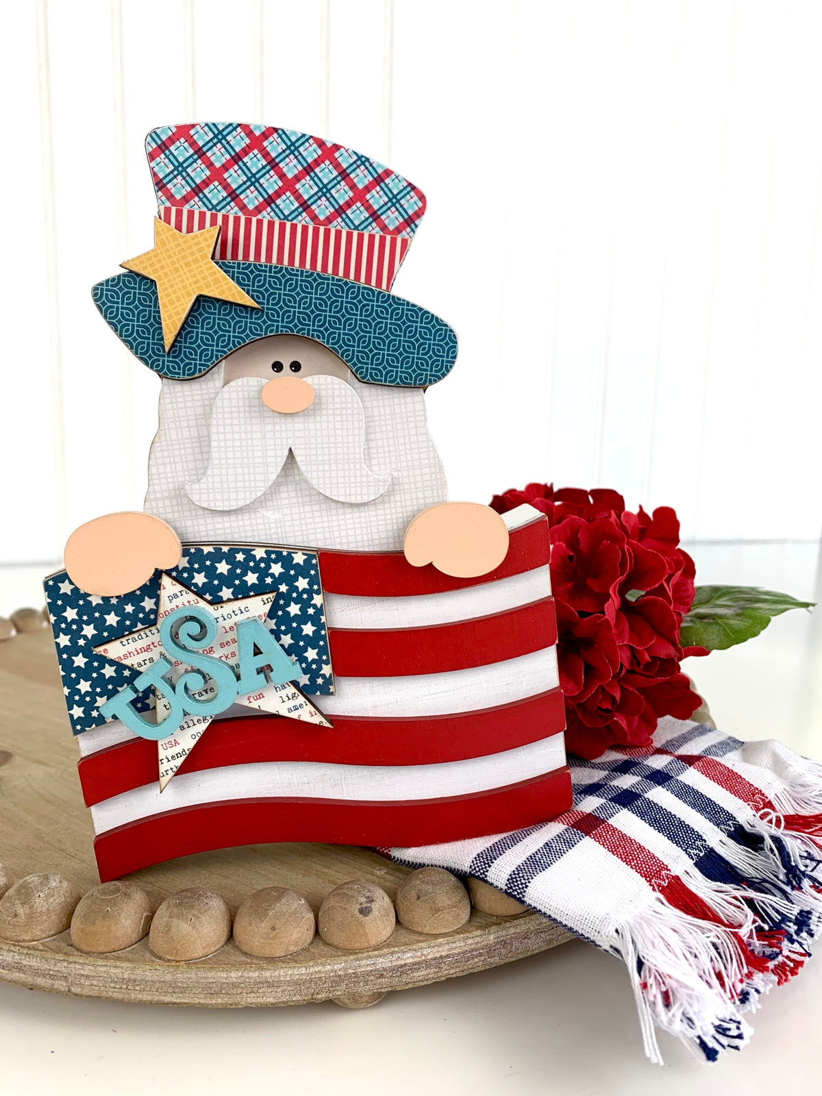 Wood Uncle Sam decoration holding an American flag sitting on a wood tray with a red flower