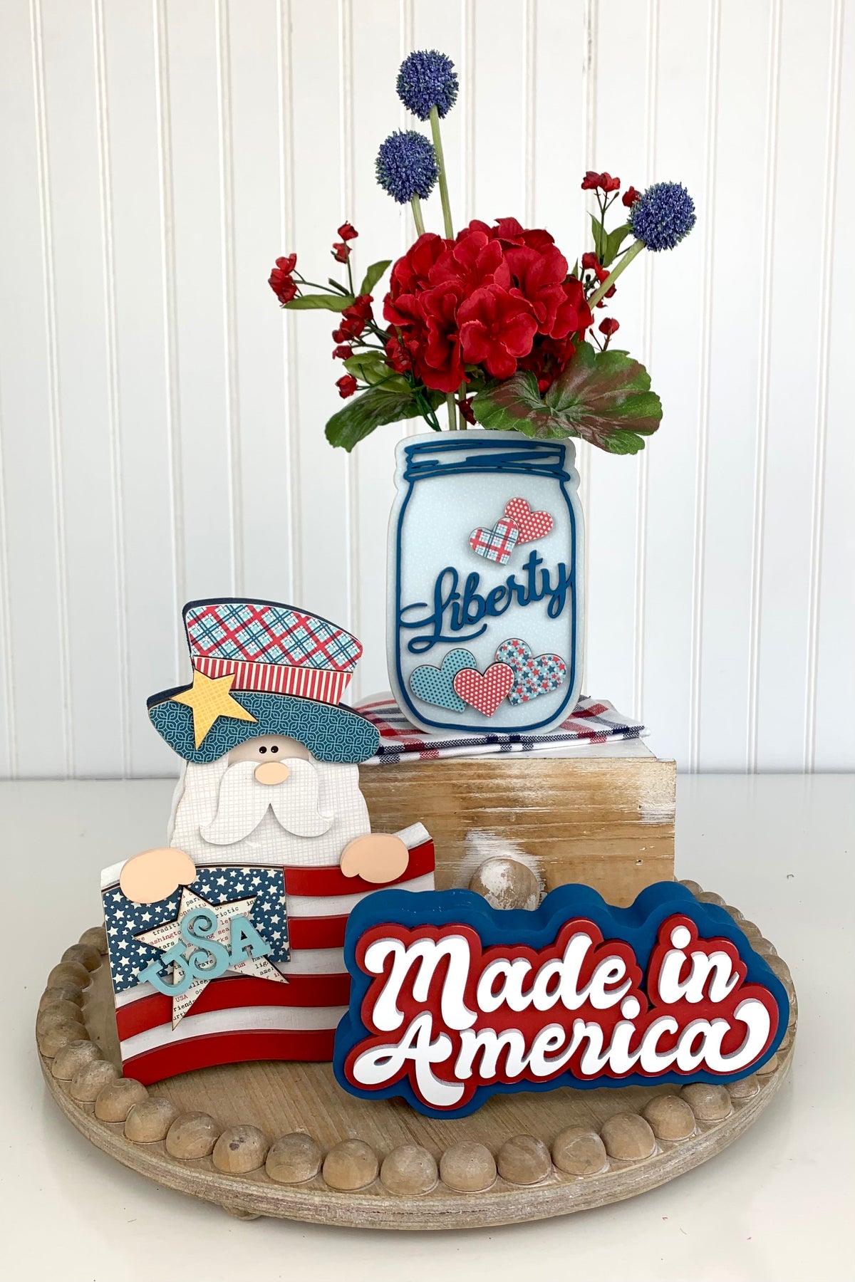 Wood tray with 4th of July wood decorations with an uncle sam holding a flag, a mason jar with liberty and hearts, and a made in america wood cutout sign