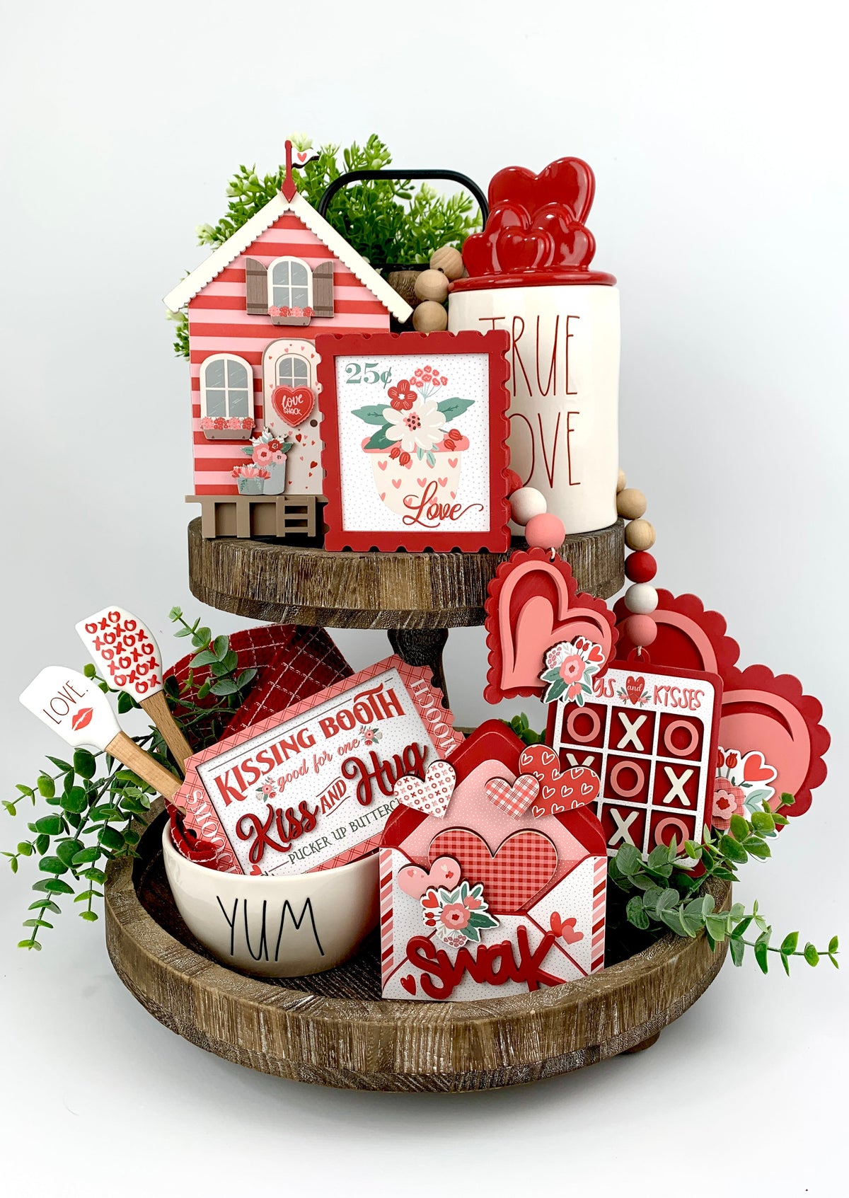 Valentine theme tiered tray decorations in pink and red; kissing booth ticket, tic tac toe garland, love shack, love stamp and envelope. 