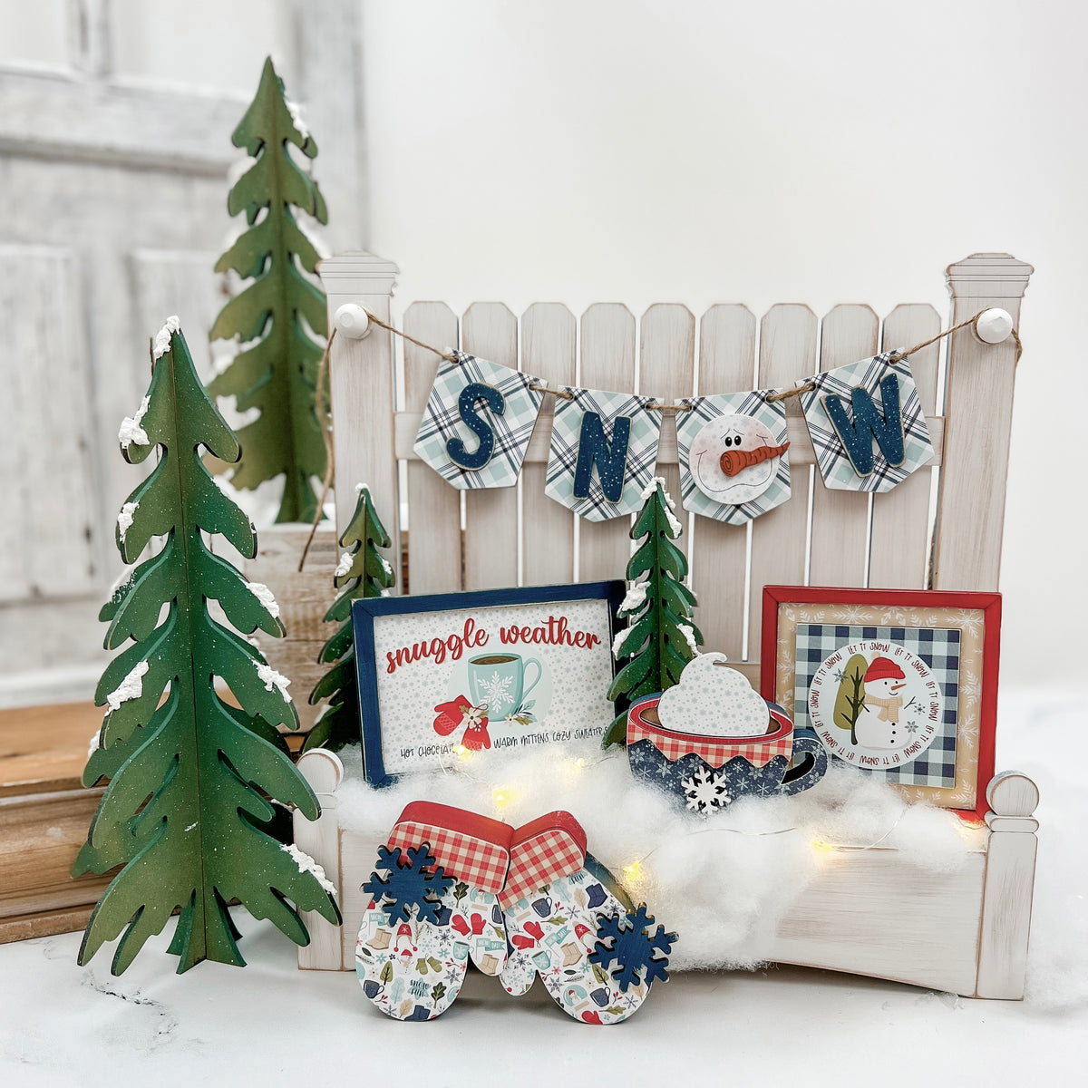 Winter-themed DIY wood craft kit decor with Christmas trees, 'SNOW' banner, and festive items on a white surface.