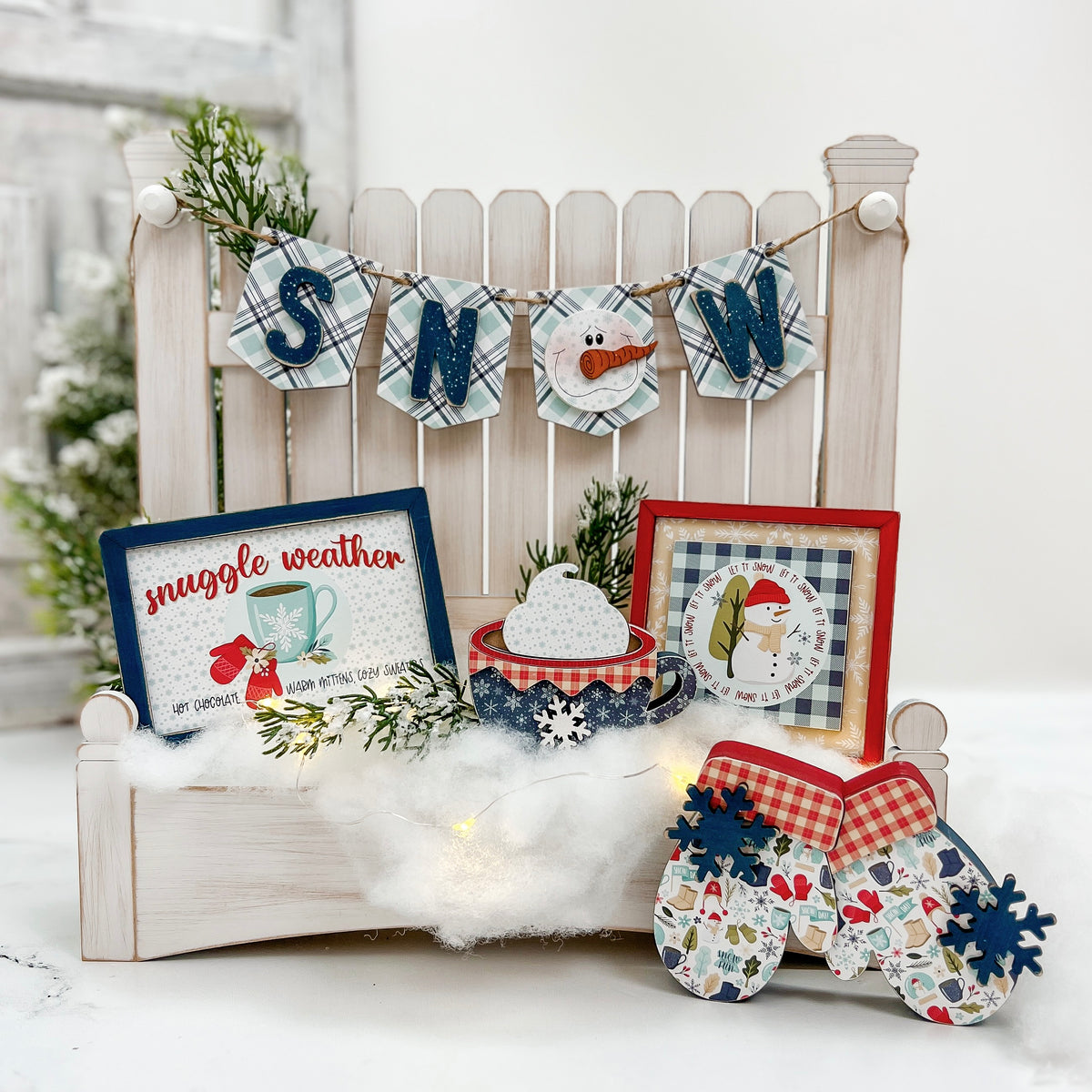 DIY wood decor kit with decorative winter scene with signs, mittens, and a snowman on a white bench.