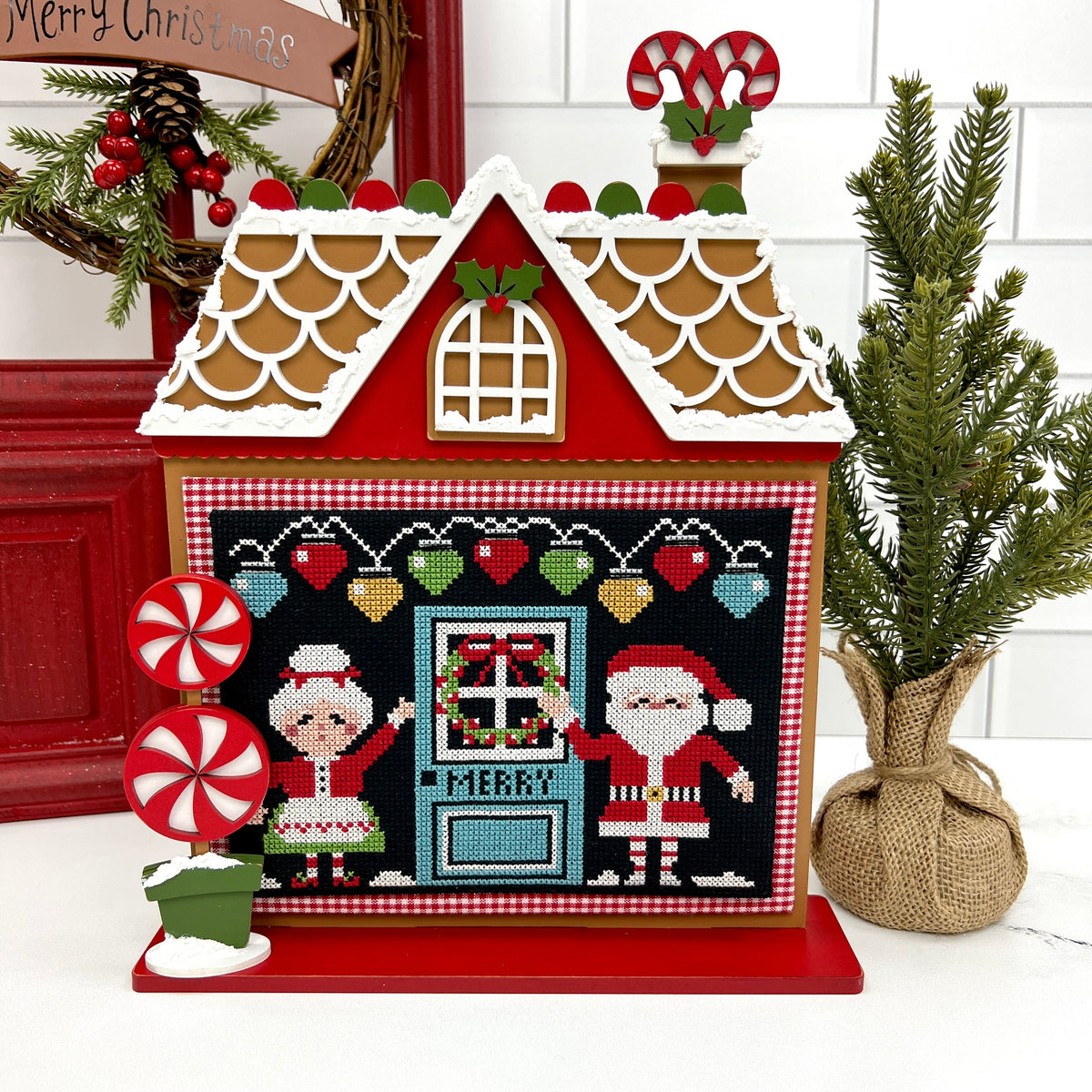 Wood gingerbread house cross stitch display shown with the Christmas aDOORables by Stitching with the Housewives.