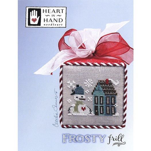 Cross-stitched design of a snowman and house with a red bow on a blue background, featuring 'Heart in Hand' brand.