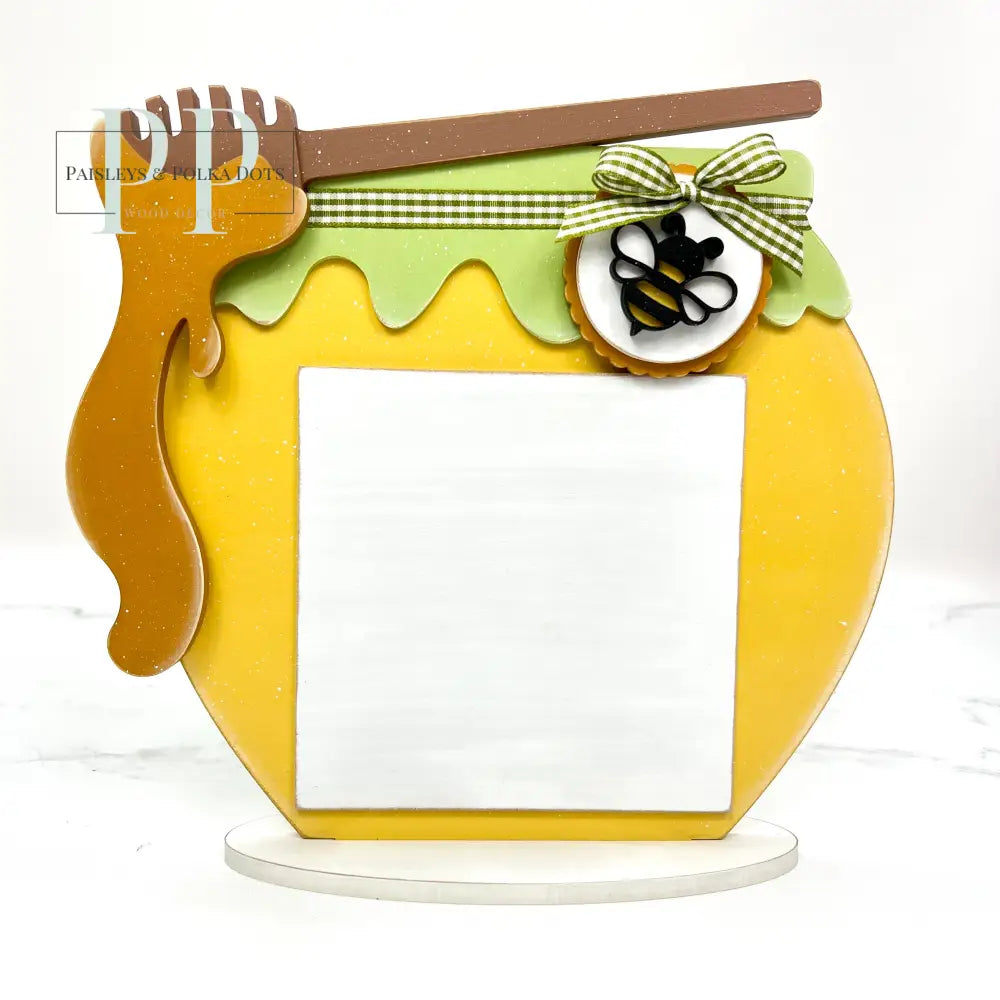 Wood honey jar with a honey dipper on top with dripping honey for displaying a finished cross stitch piece