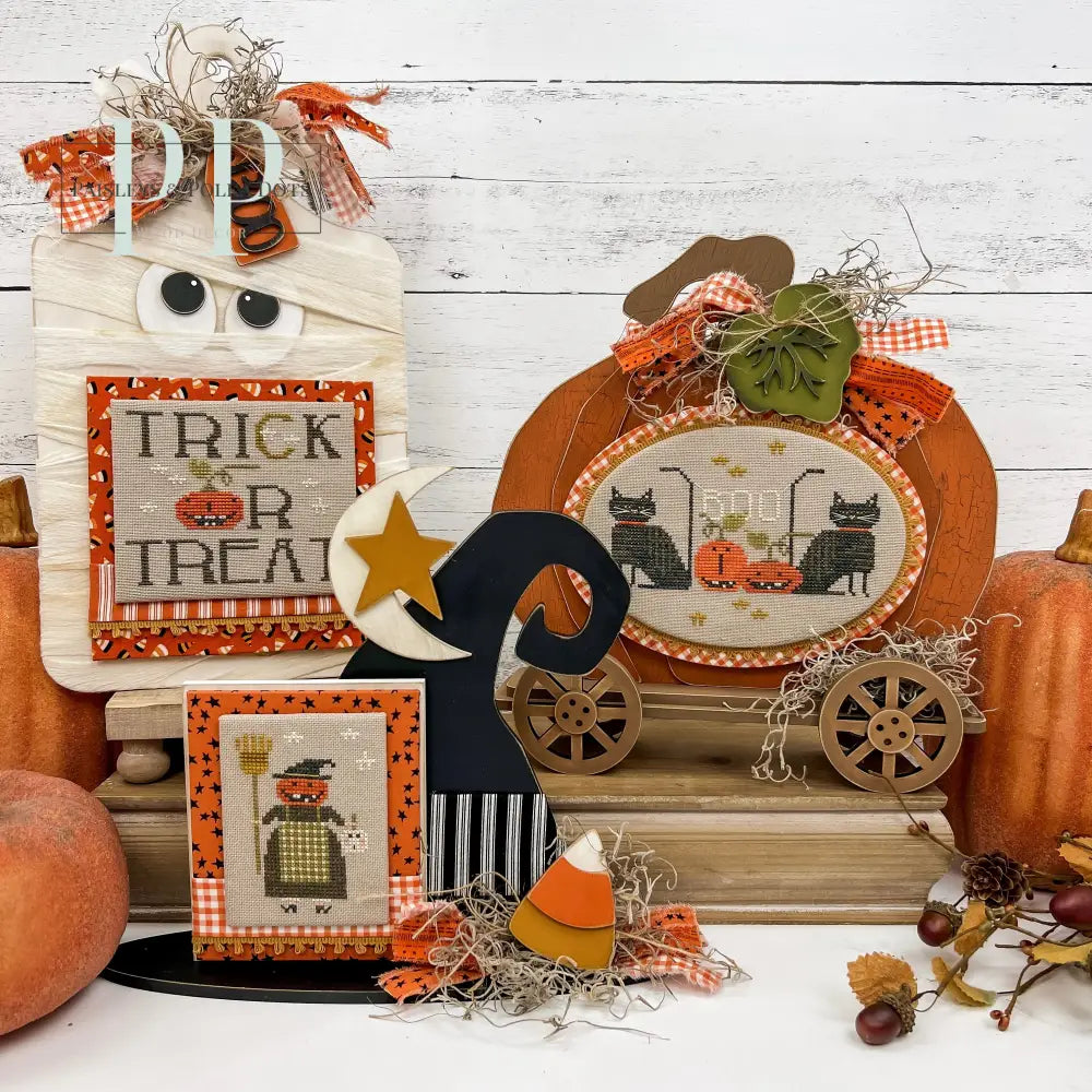 Halloween themed cross stitch display boards; mummy, witch hat, and primitive pumpkin with wheels. Finished halloween cross stitch designs by Brenda Gervais.