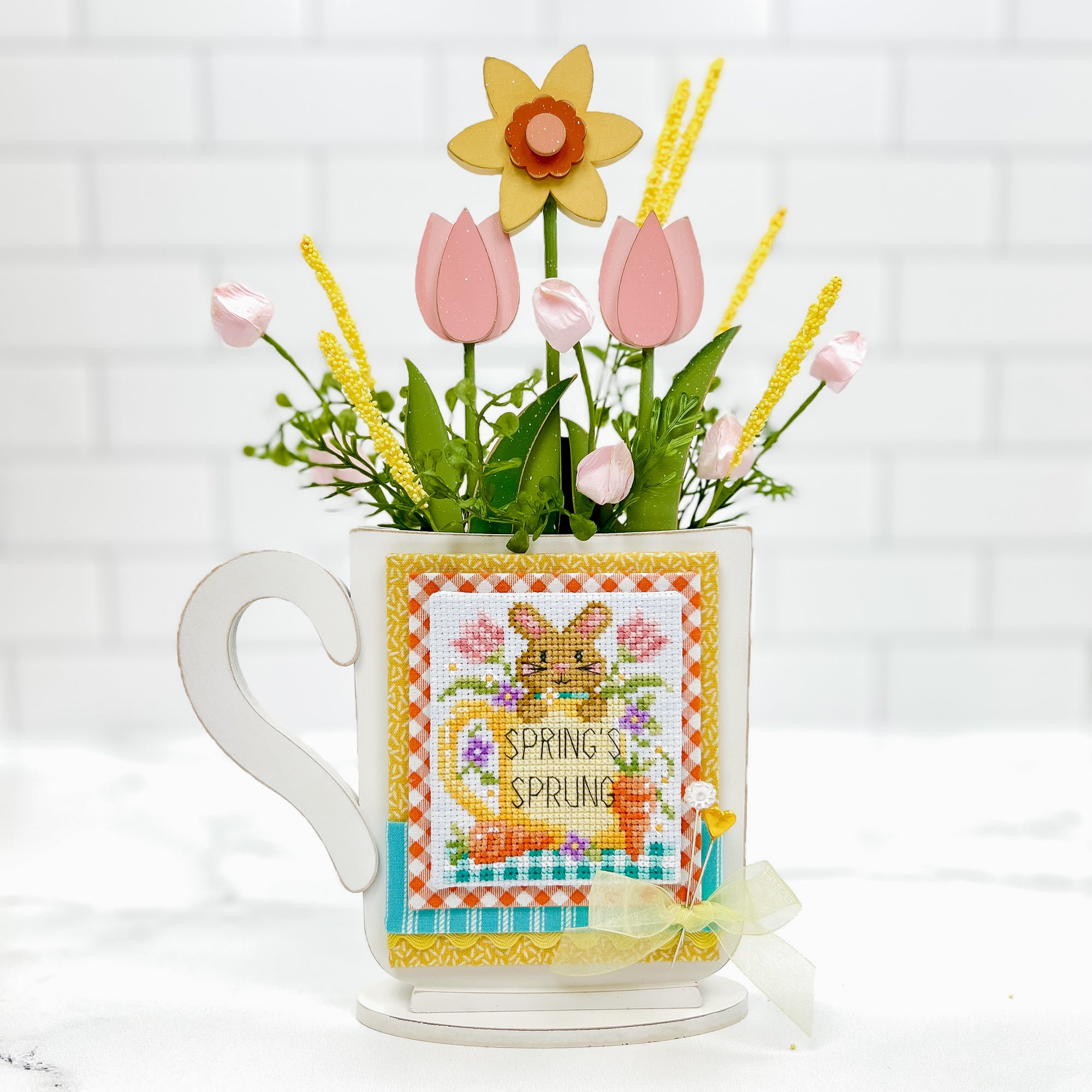 Mug cross stitch display with spring tulips and daffoldile inside the mug. Cross stitch pattern by Shannon Christine Designs